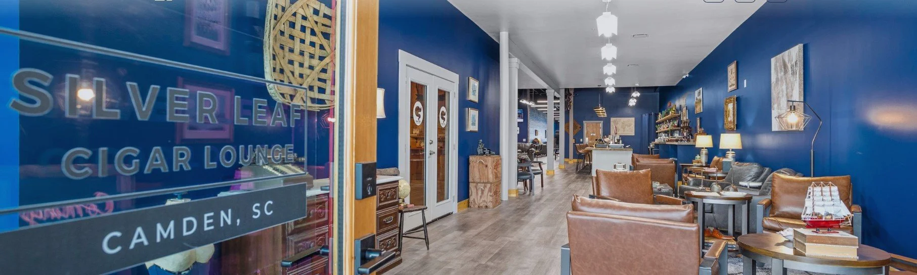 Interior of Silver Leaf Cigar Lounge in Camden, South Carolina, featuring blue walls, leather armchairs, coffee tables, decorative pictures, lamps, and a ship model on one table.