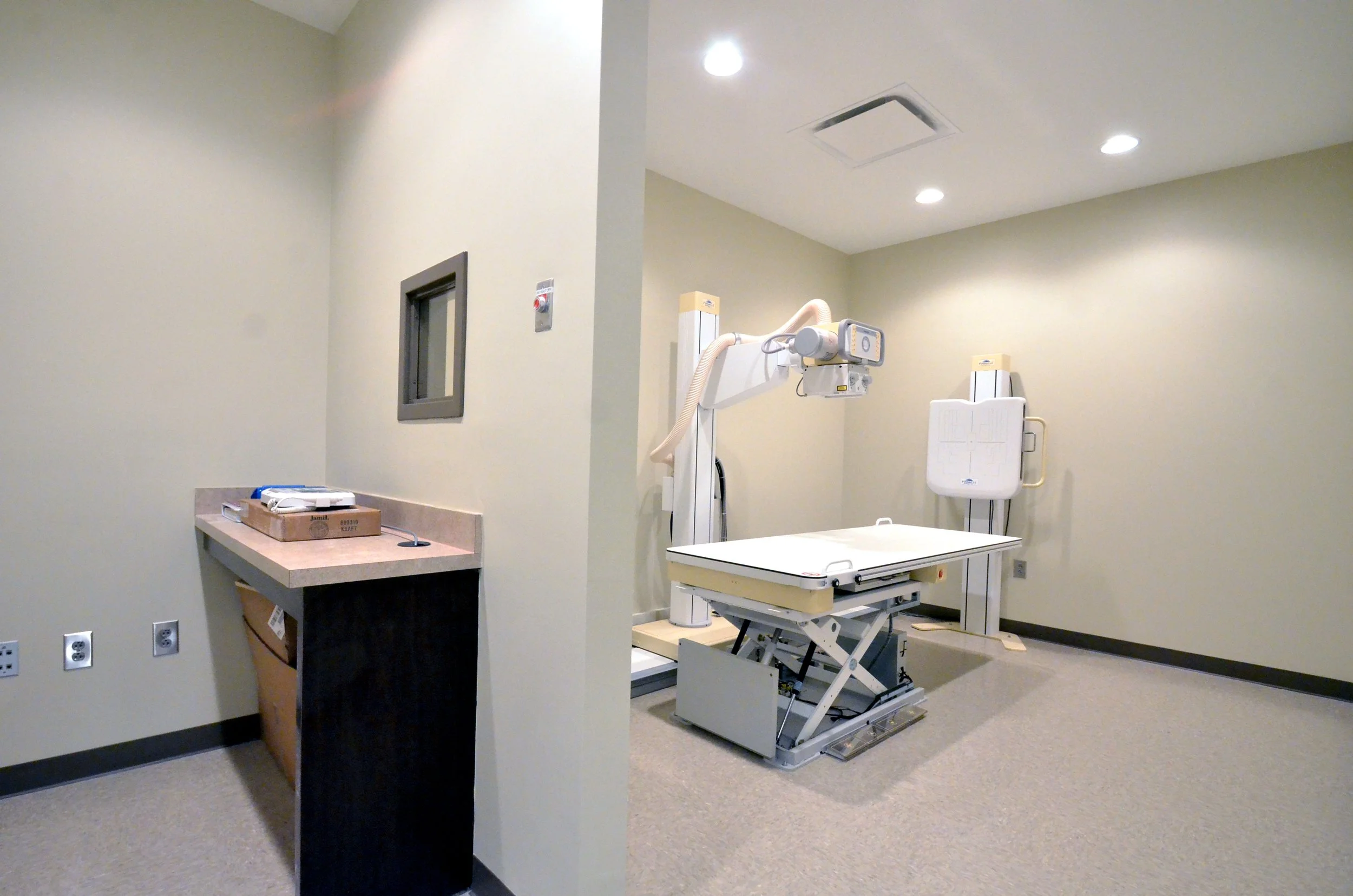 Hospital room with X-ray machine, examination table, medical equipment, and a small table with a box on it.