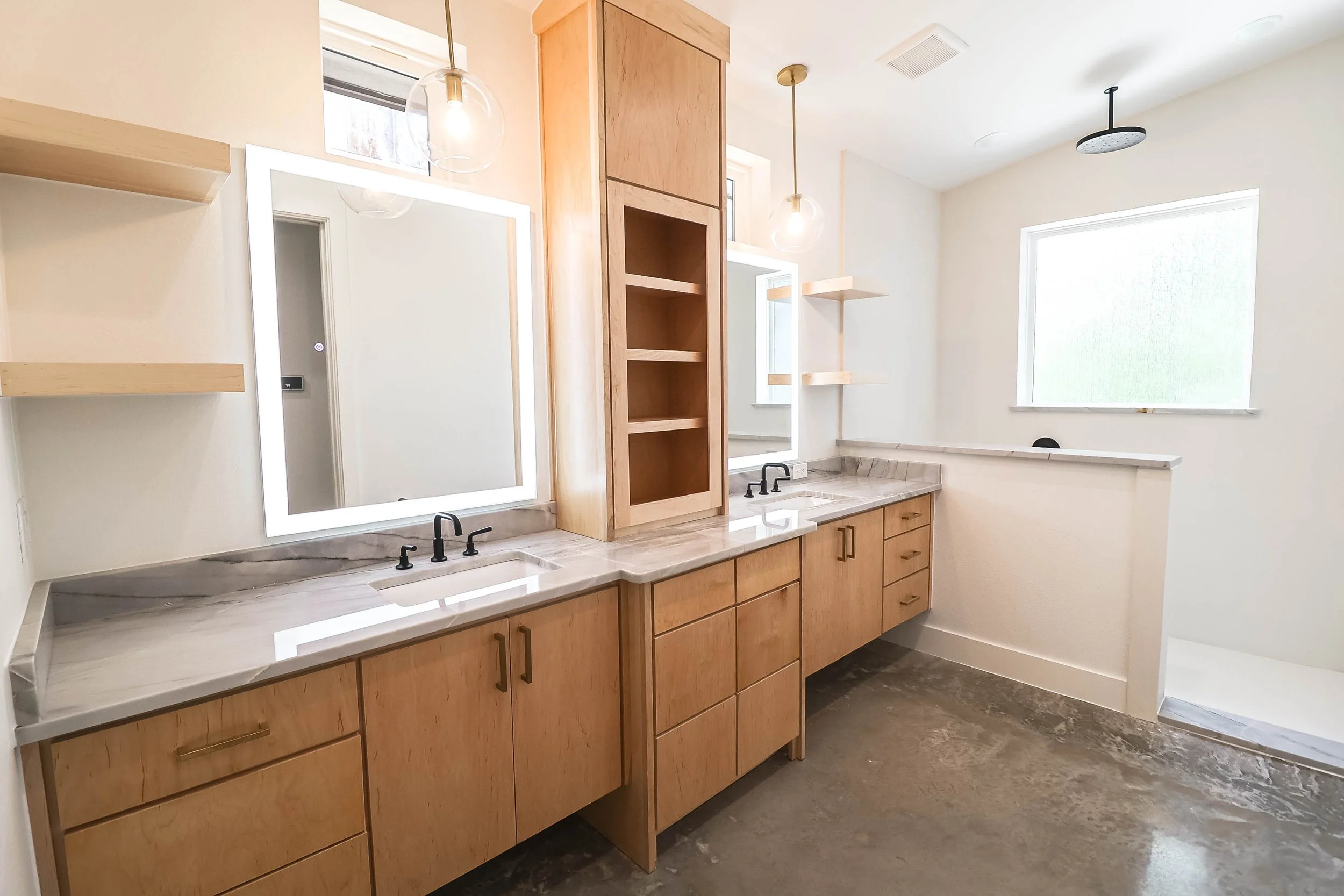 Modern bathroom with wooden cabinets, dual sinks, marble countertops, large mirror with LED lighting, wall-mounted shelves, and a window with frosted glass.