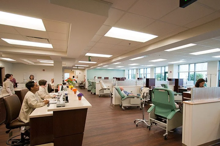 Hospital infusion center with patients receiving IV treatments in reclining chairs and healthcare staff attending to them.