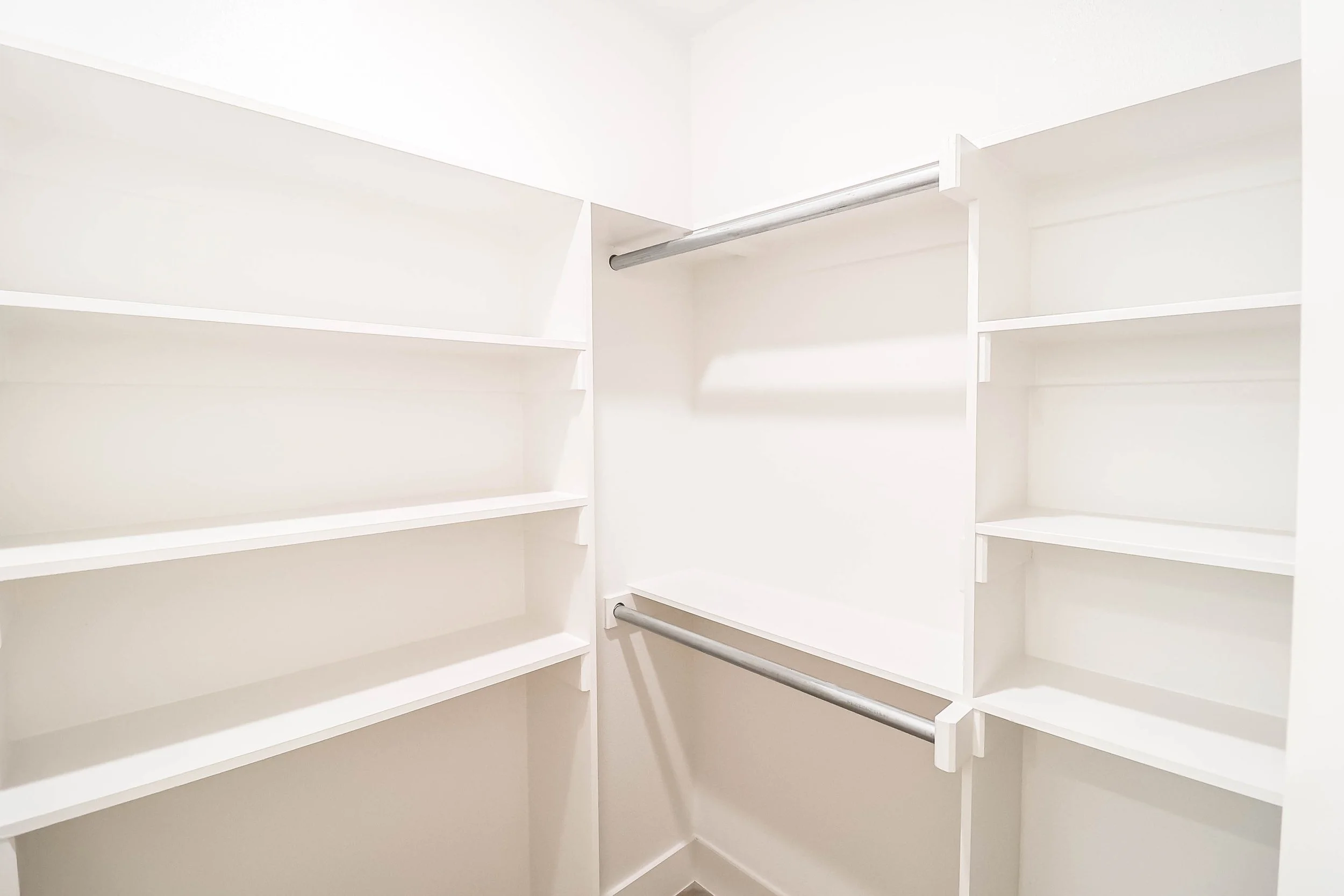 Empty white walk-in closet with multiple shelves and metal hanging rods.