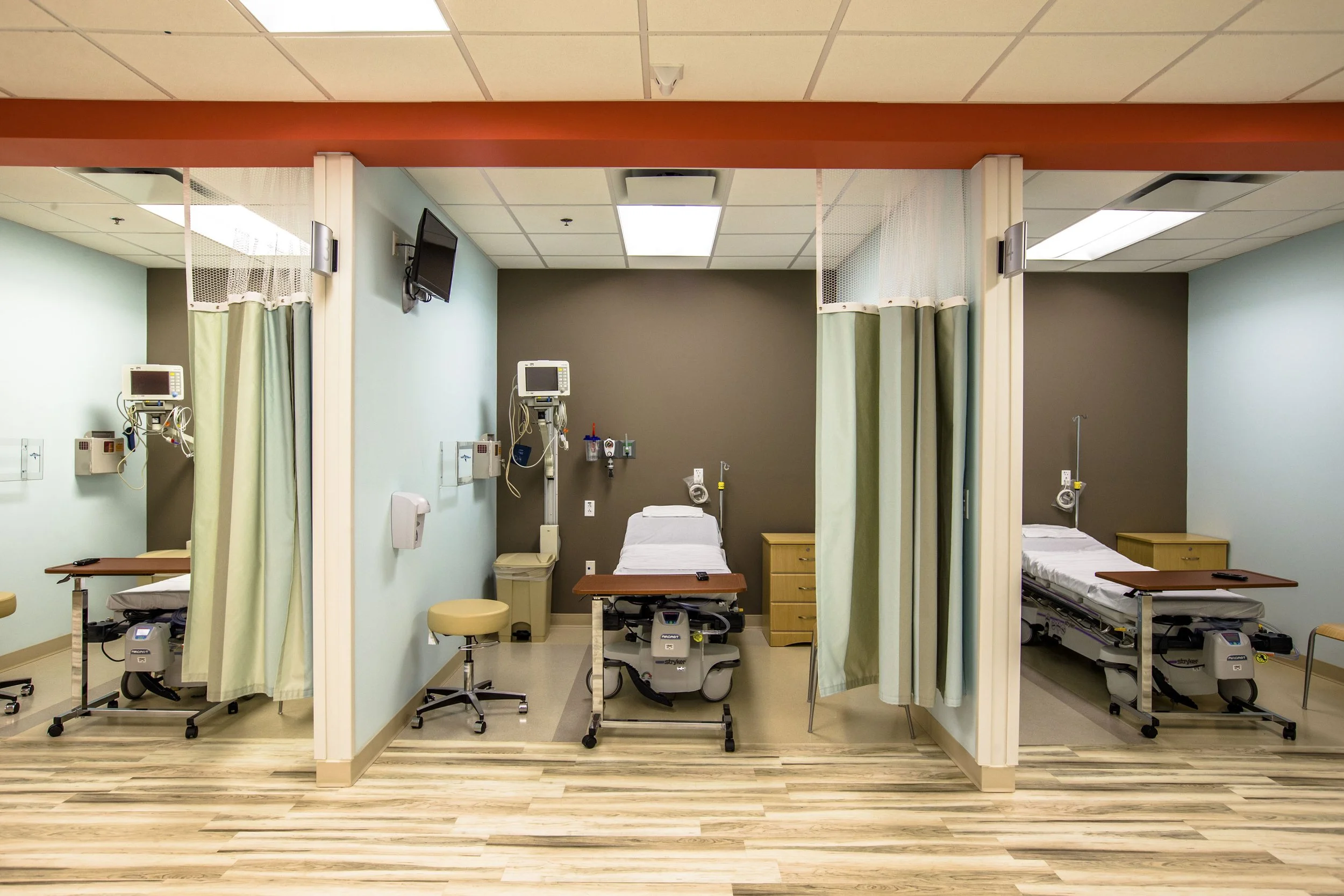 Hospital patient rooms with beds, medical equipment, and privacy curtains.