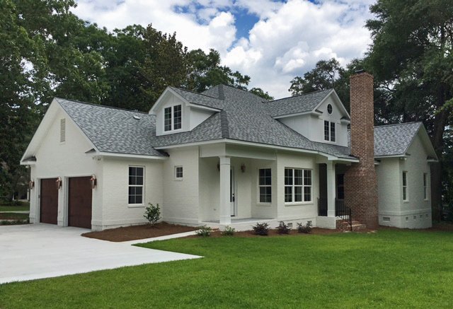 White two-story house with gray roof, attached garage, brick chimney, front porch, and well-maintained lawn.