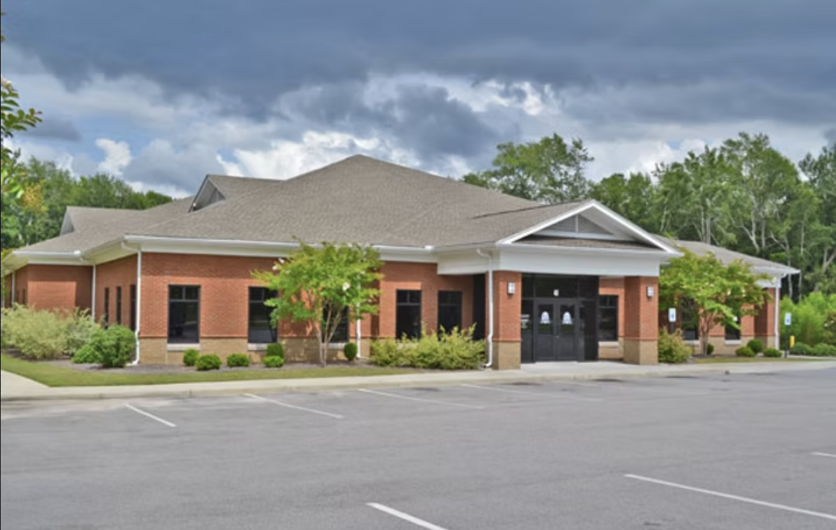A brick restaurant in a suburban area with a parking lot in front and trees surrounding the building.