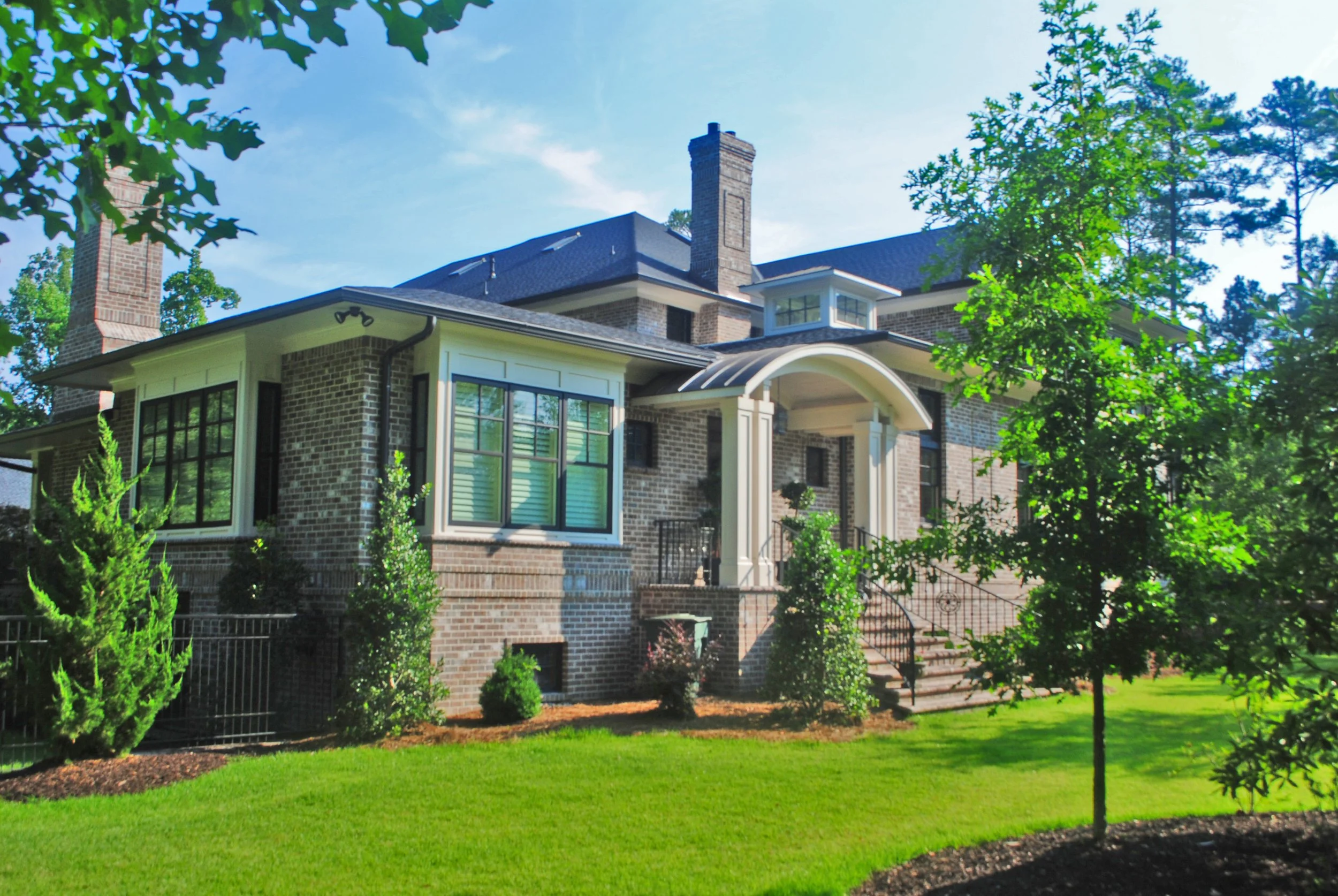 Large brick house with multiple chimneys, surrounded by green trees and a well-maintained lawn.