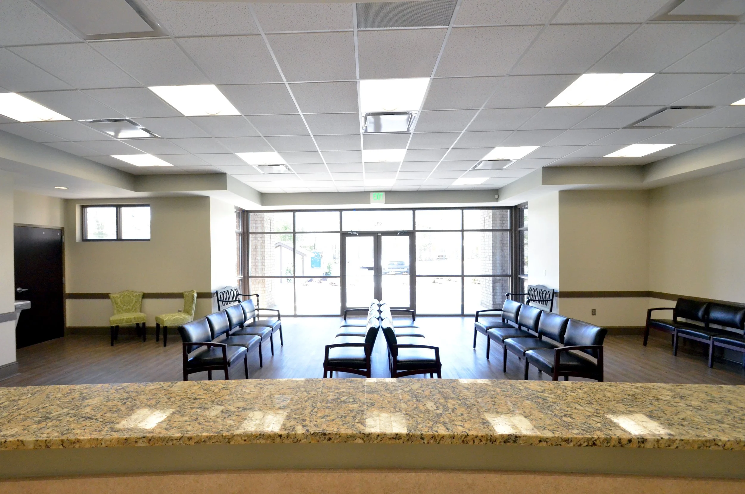 Waiting room or lobby with rows of chairs, large windows with glass doors, and a granite countertop in the foreground.