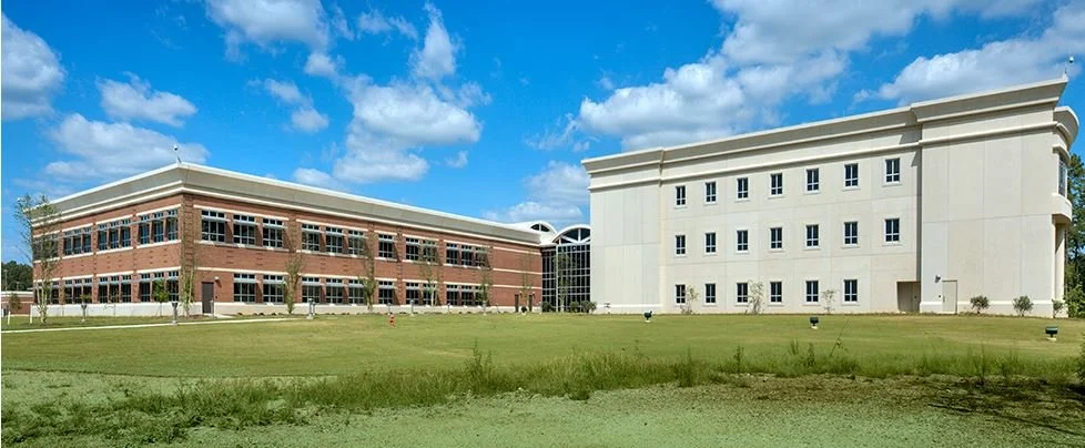 Photo of two large buildings with a grassy area in front, under a partly cloudy sky.