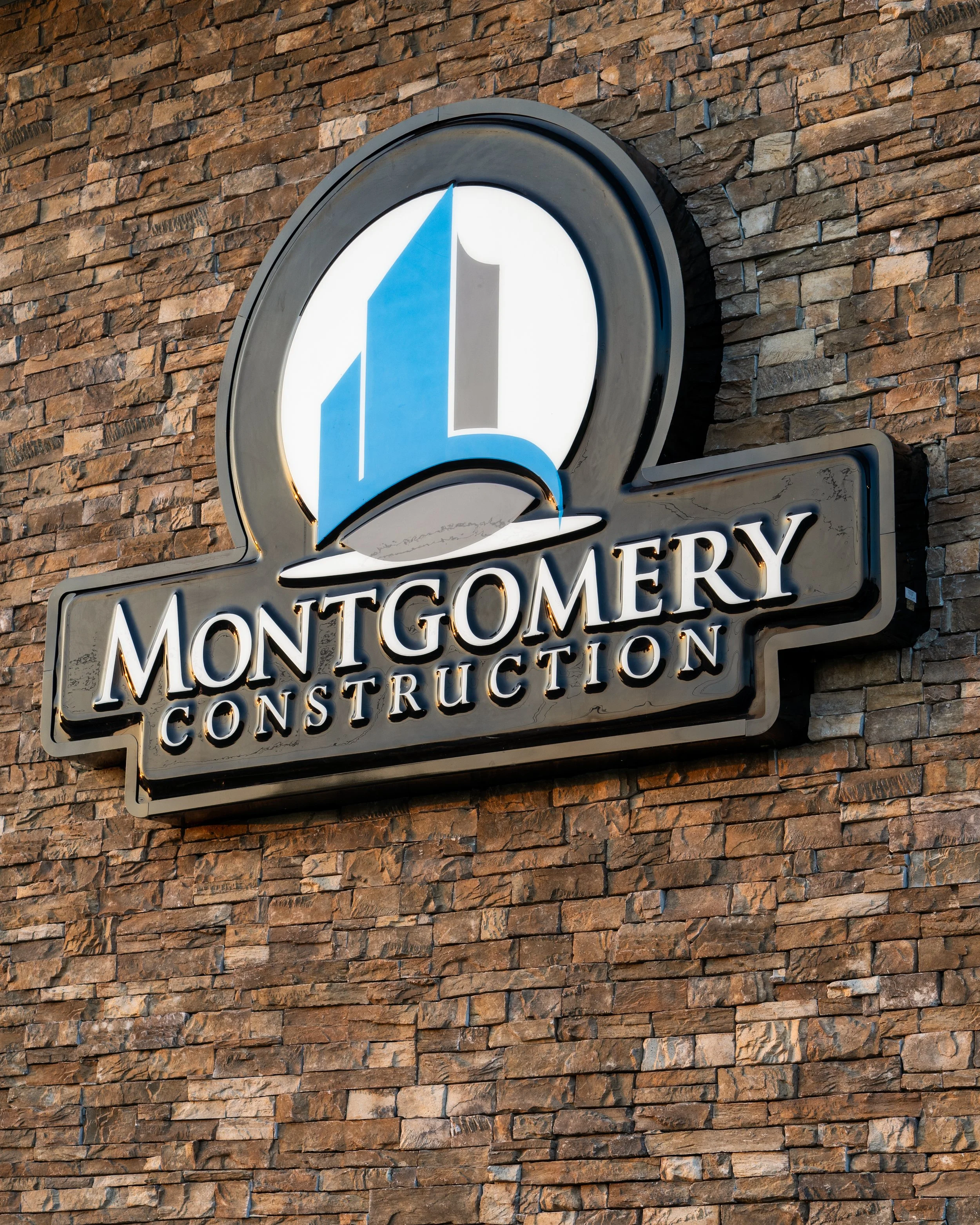 Close-up of a Montgomerie Construction sign mounted on a brick wall. The sign features a large stylized number '1' with a blue and gray design.