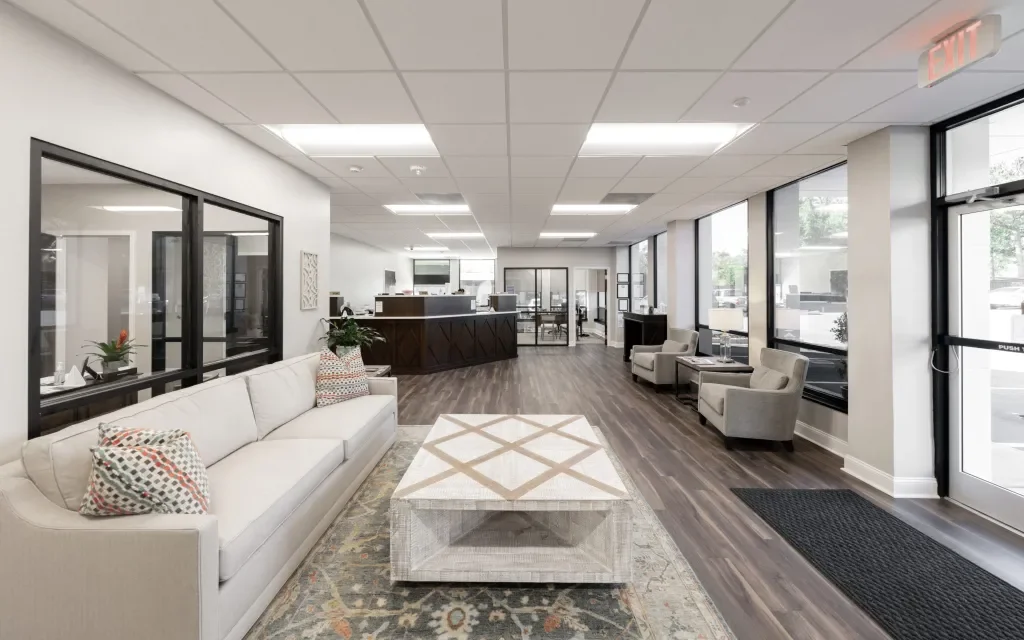 Modern lobby with white sofa, armchairs, coffee table, large windows, and reception desk