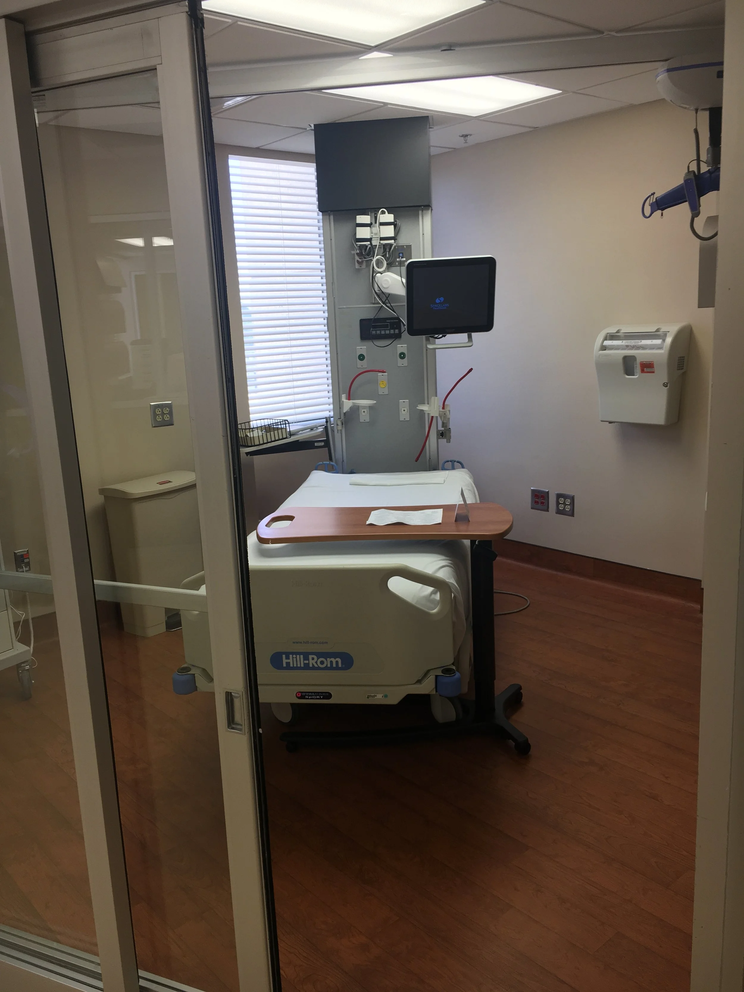 Hospital room with medical equipment, a hospital bed with an adjustable tray, a monitor, and a privacy curtain.
