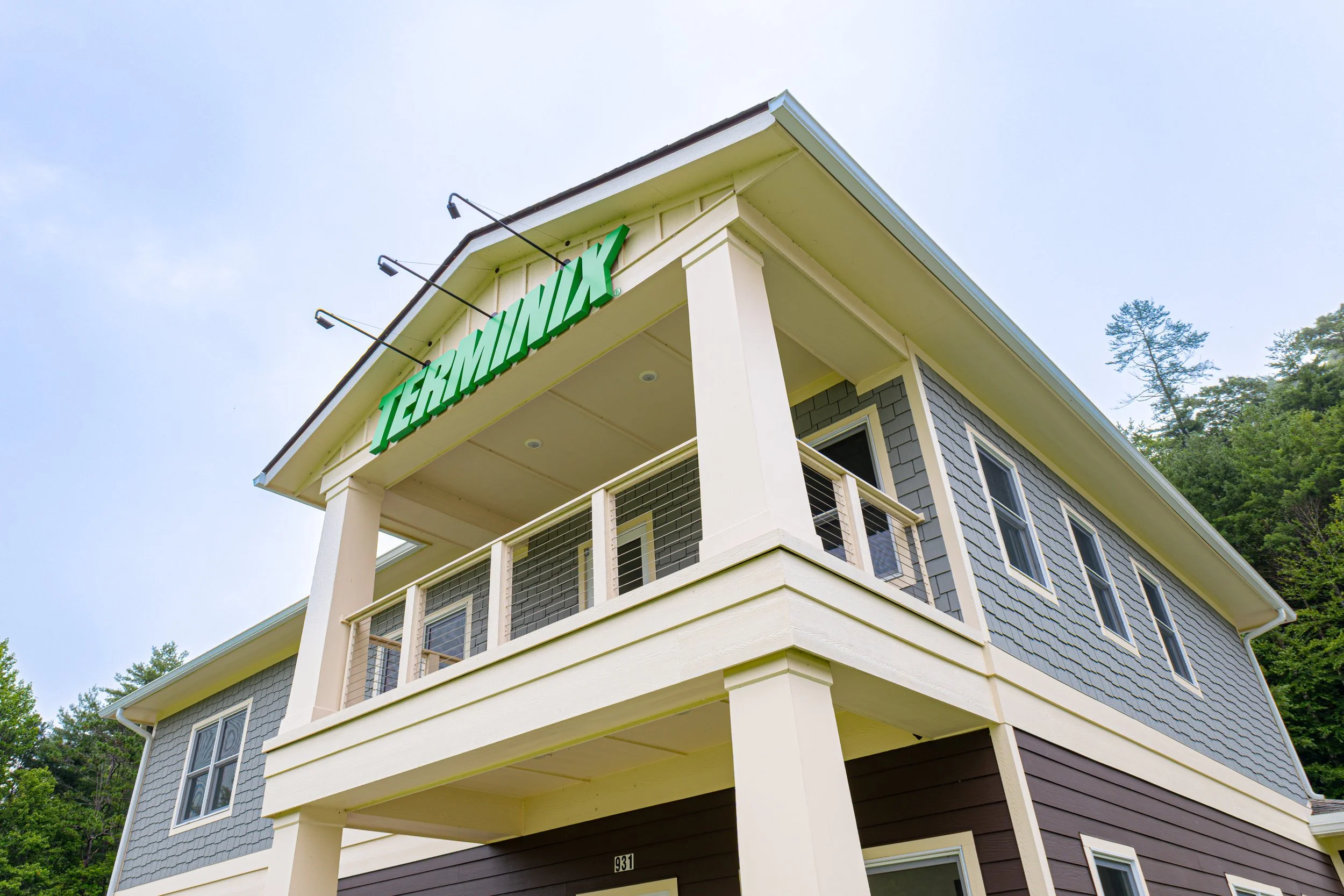 A multi-level house with gray siding and white trim, marked "TERRAMAX," is shown from a low angle against a blue sky with trees on the right side.