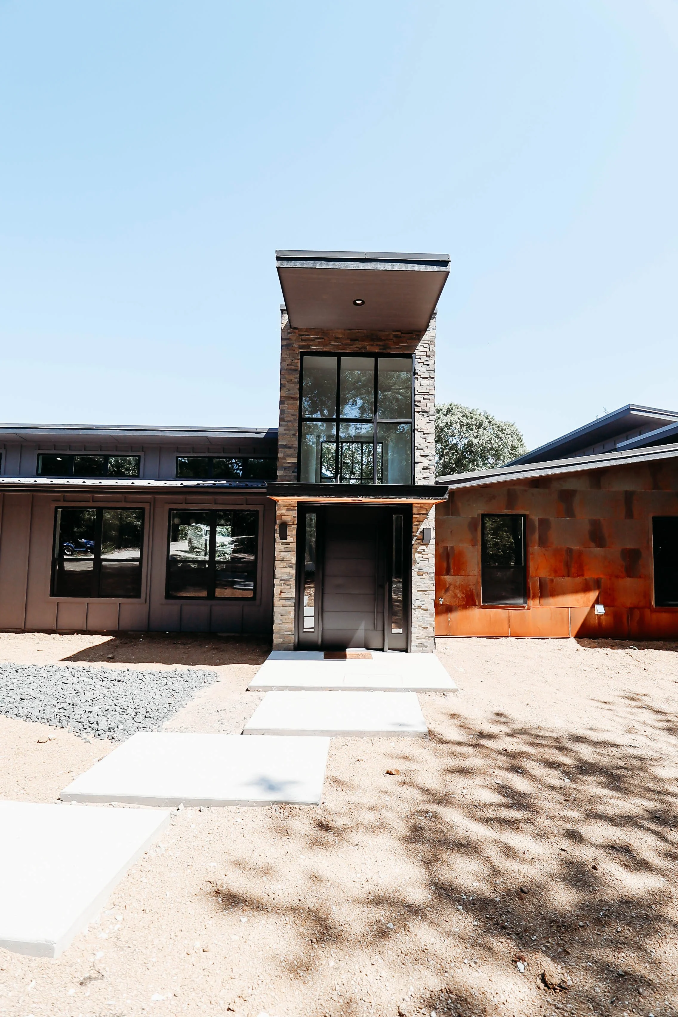 Modern house with a stone and glass facade, concrete steps leading to the door, and a clear blue sky background.
