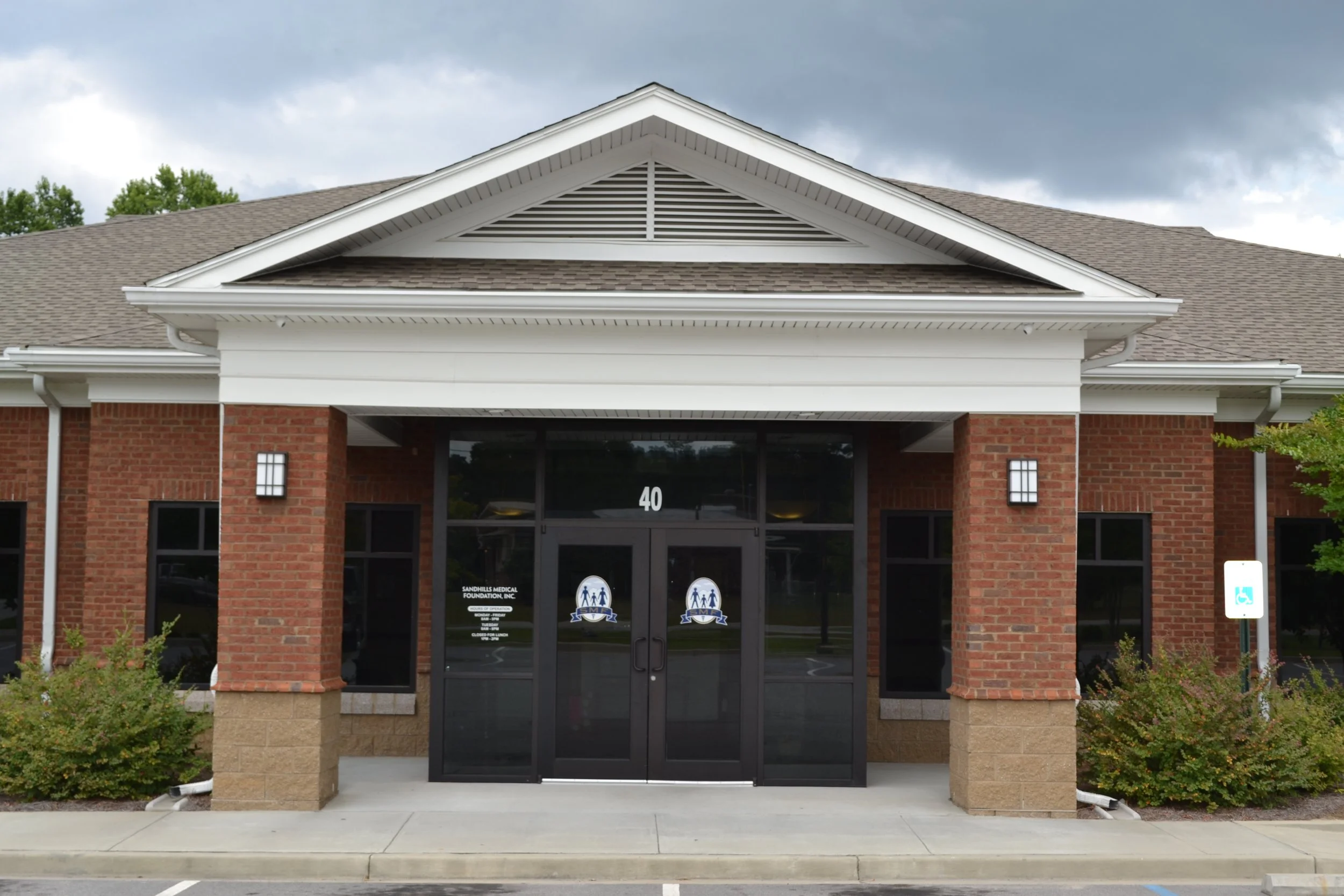 Front entrance of a brick building with glass doors and the number 40 above. There are signs indicating a medical foundation, and accessibility features near the sidewalk.