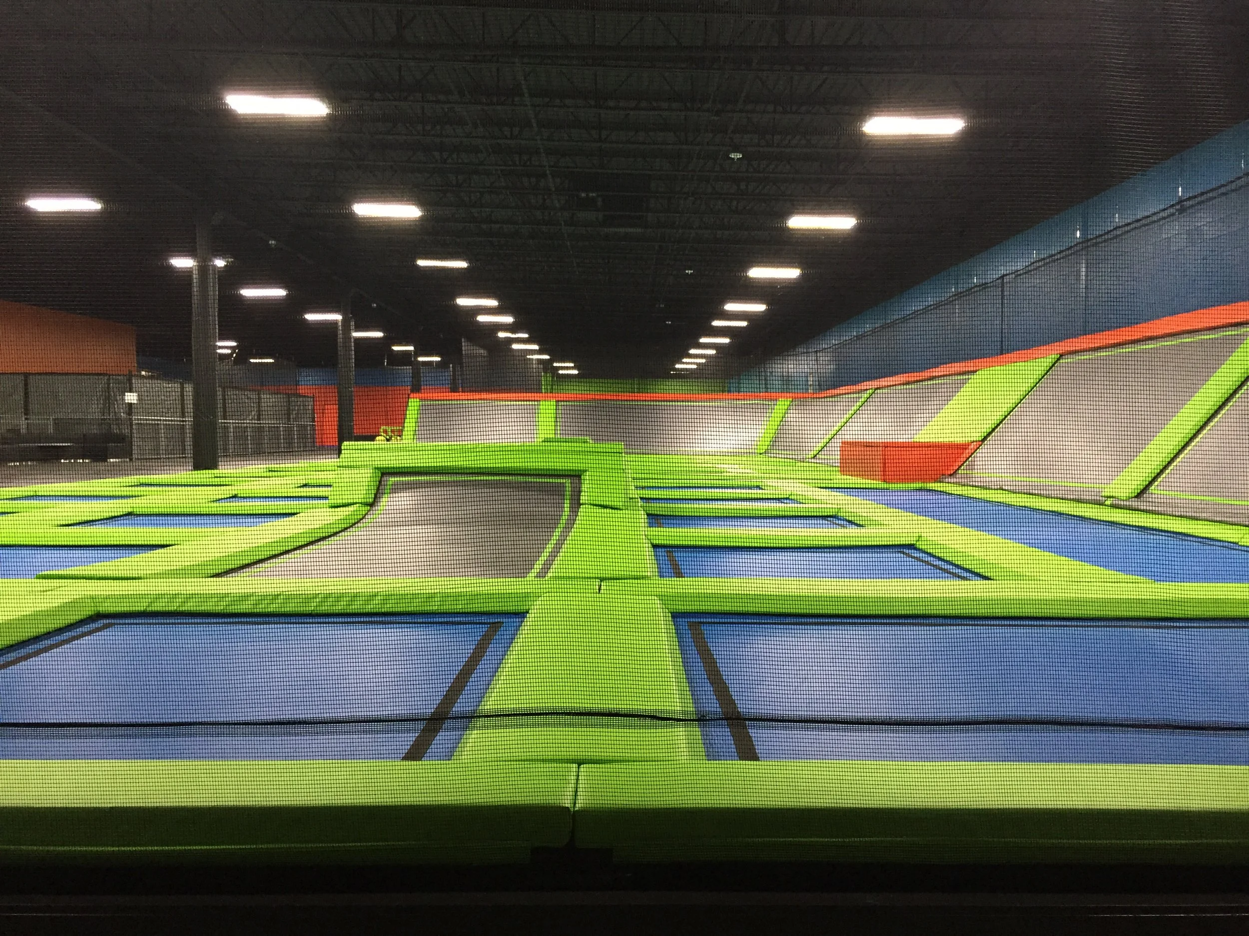 An indoor trampoline park with multiple trampolines, colorful padded areas, and a secured net enclosure for safety.