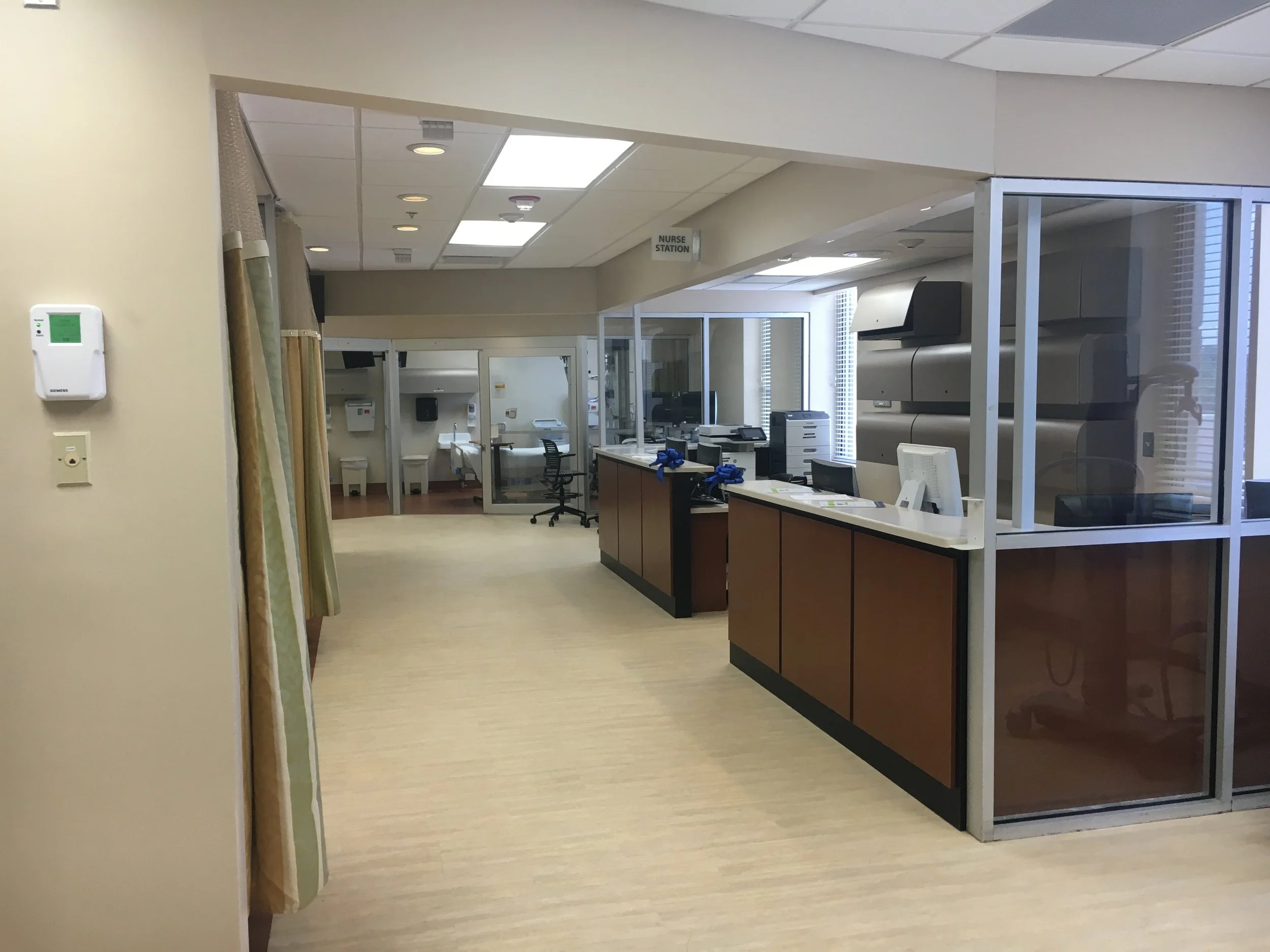 Hospital corridor with a nurses' station, medical equipment, and chairs.