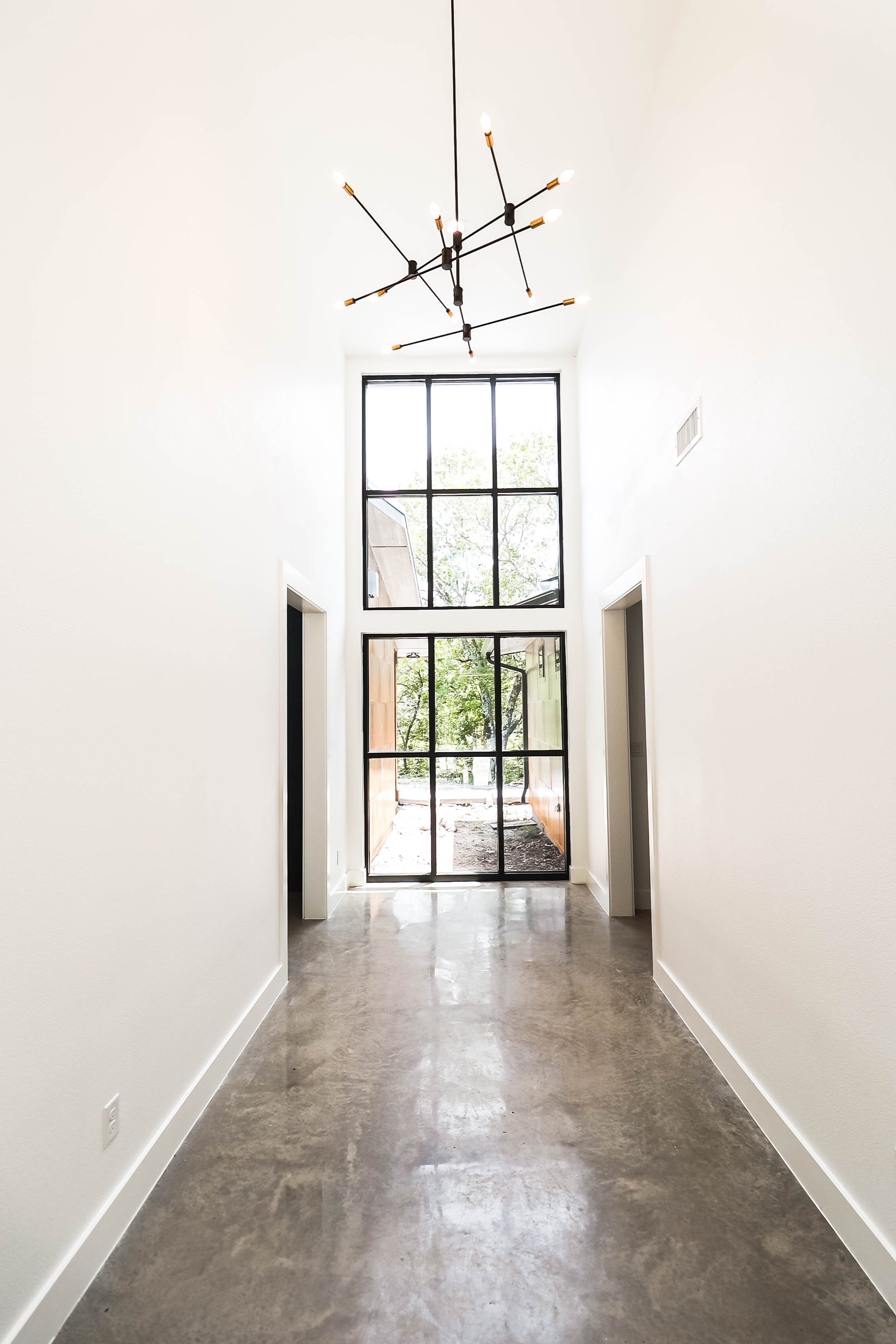 A modern, minimalistic hallway with white walls, polished concrete floor, and large glass doors at the end.
A contemporary chandelier with multiple exposed bulbs hangs from the ceiling.