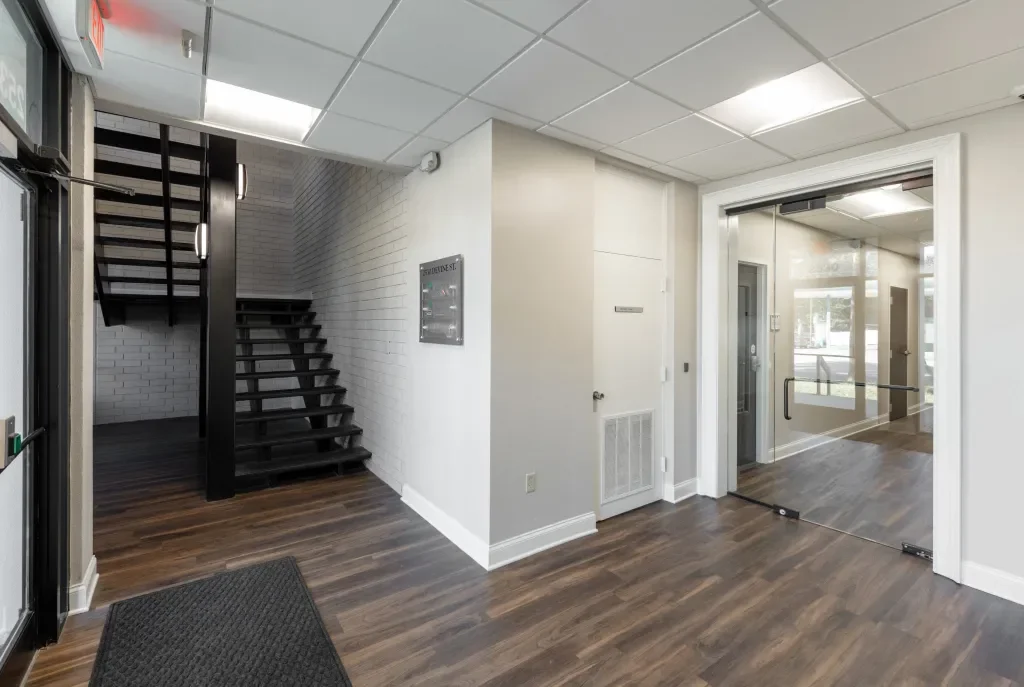 Interior of a modern office building with a staircase, glass doors, and wooden flooring.