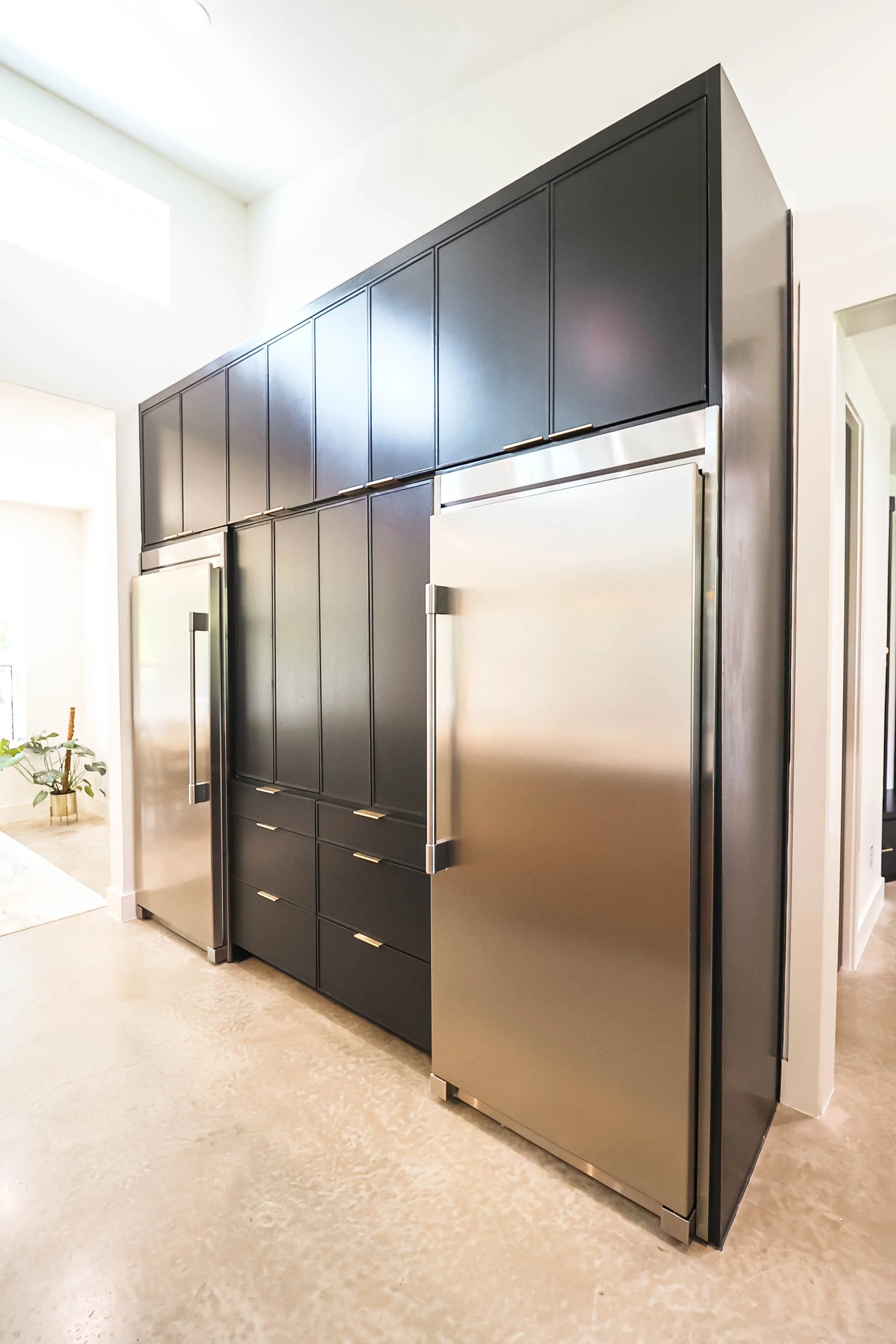 Modern kitchen with black cabinetry above and below, and stainless steel refrigerator, with a beige tiled floor and white walls.