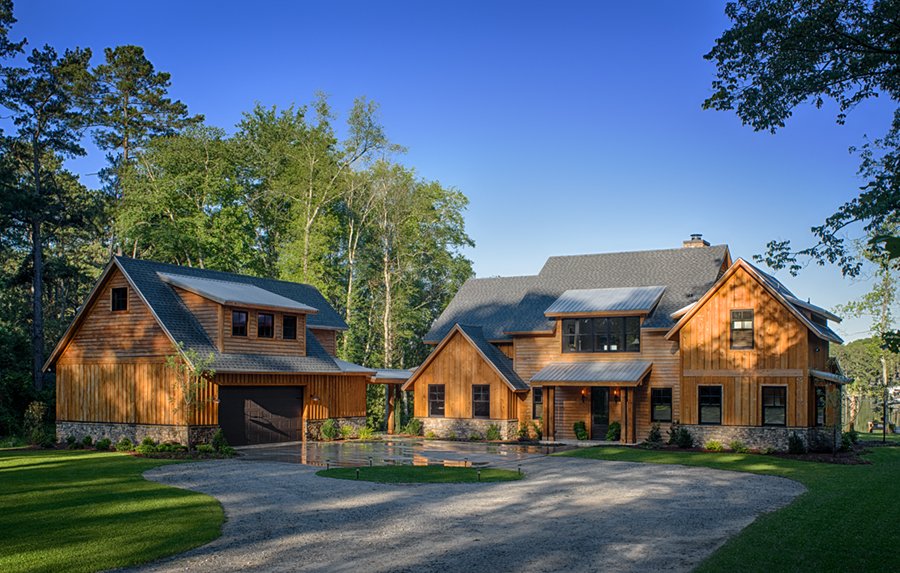 Large wooden house with multiple sections, garage, and surrounding trees, under a clear blue sky