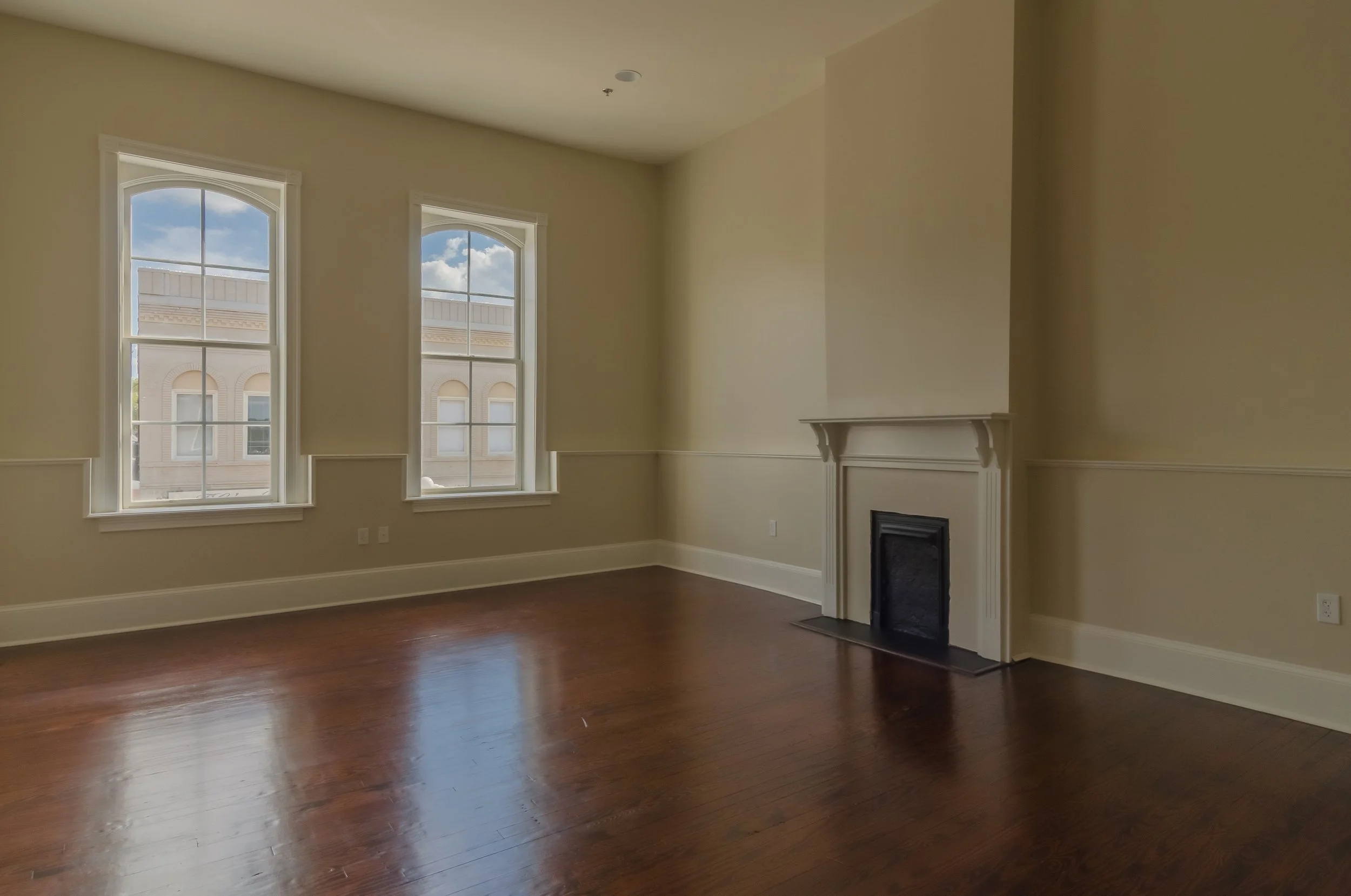 Empty room with large windows, hardwood floor, and a fireplace.