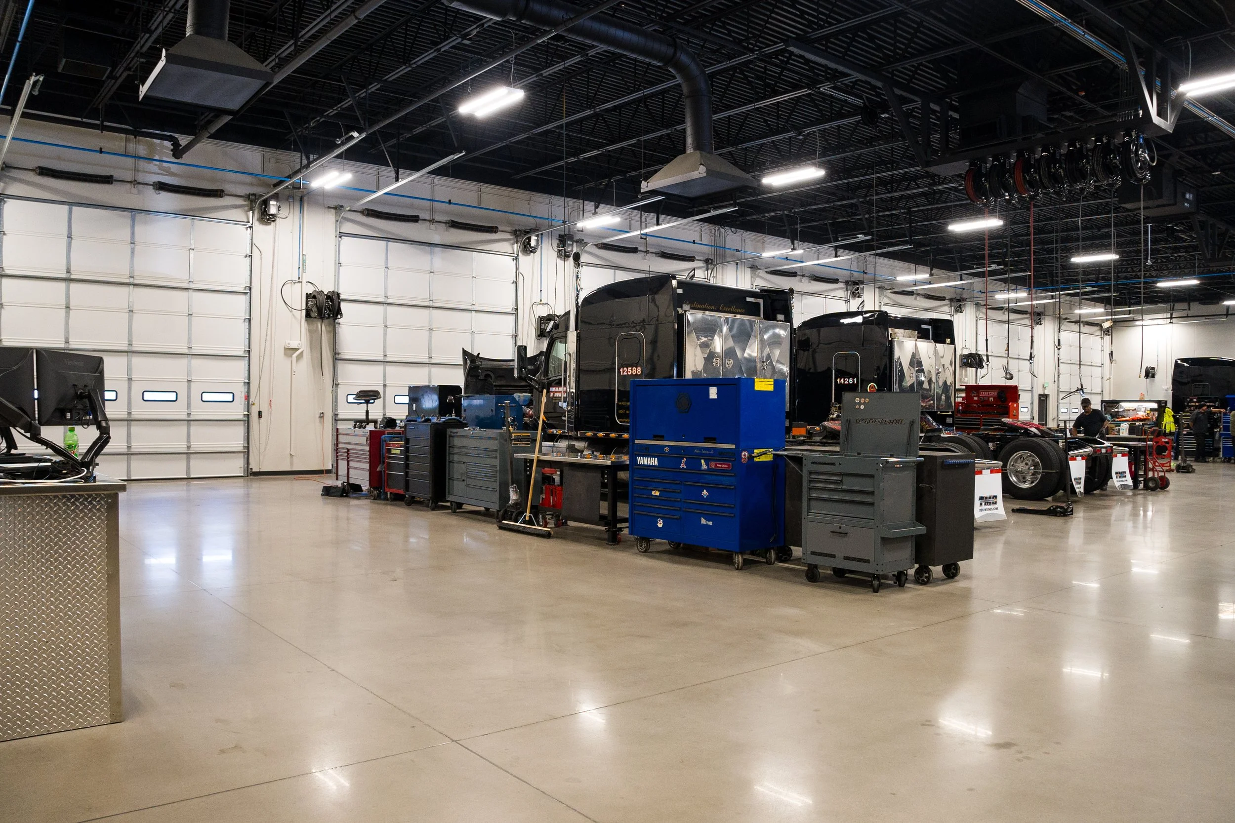 Interior of a vehicle service or repair garage with black trucks, tool chests, and workstations.