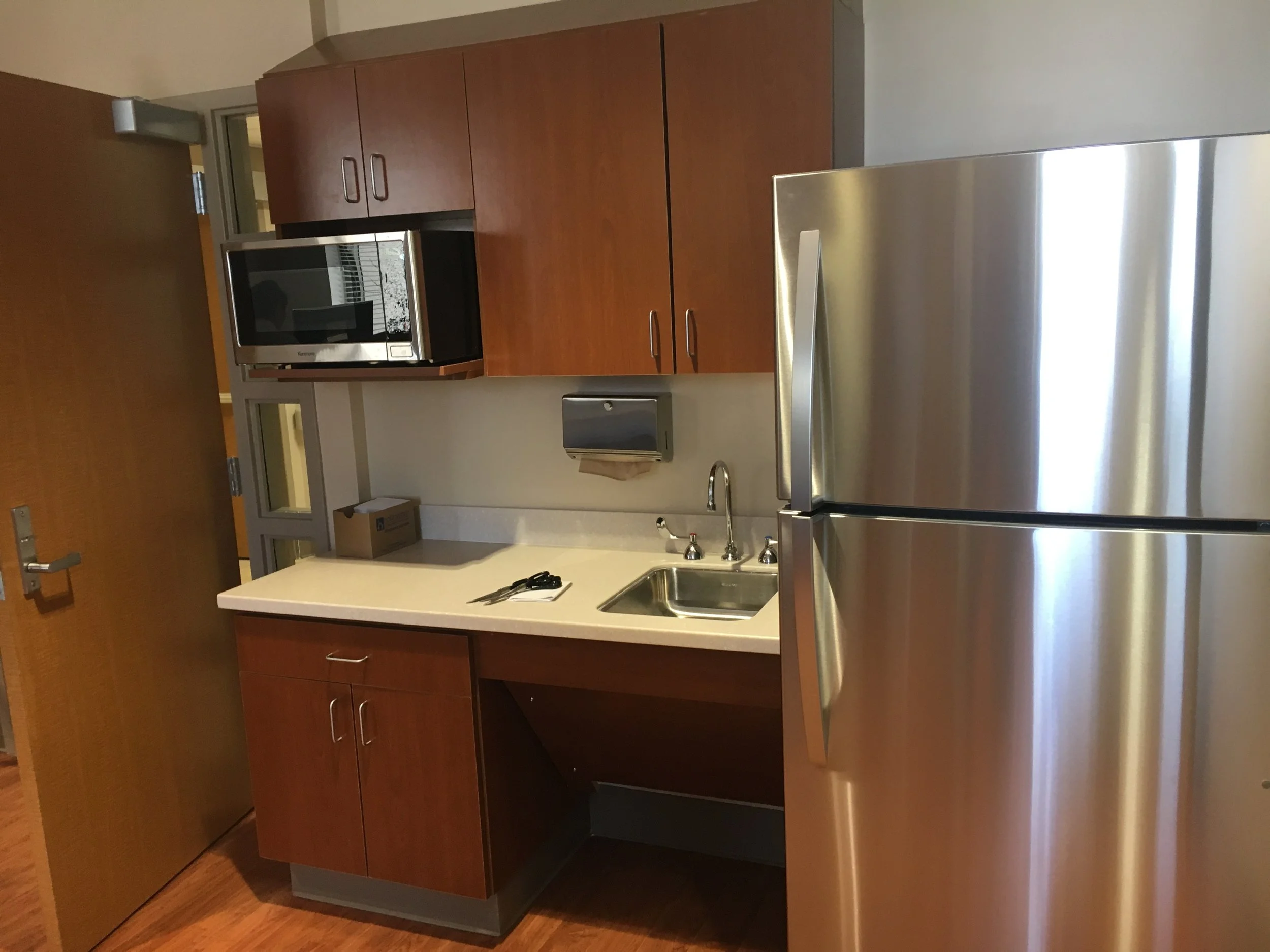 Kitchen with wooden cabinets, a microwave above the counter, a stainless steel refrigerator, a sink, and a paper towel holder.