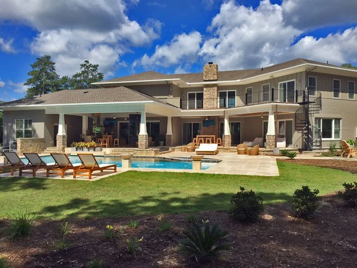 Large modern house with a backyard pool area, lounge chairs, outdoor seating, and a garden under a partly cloudy sky.