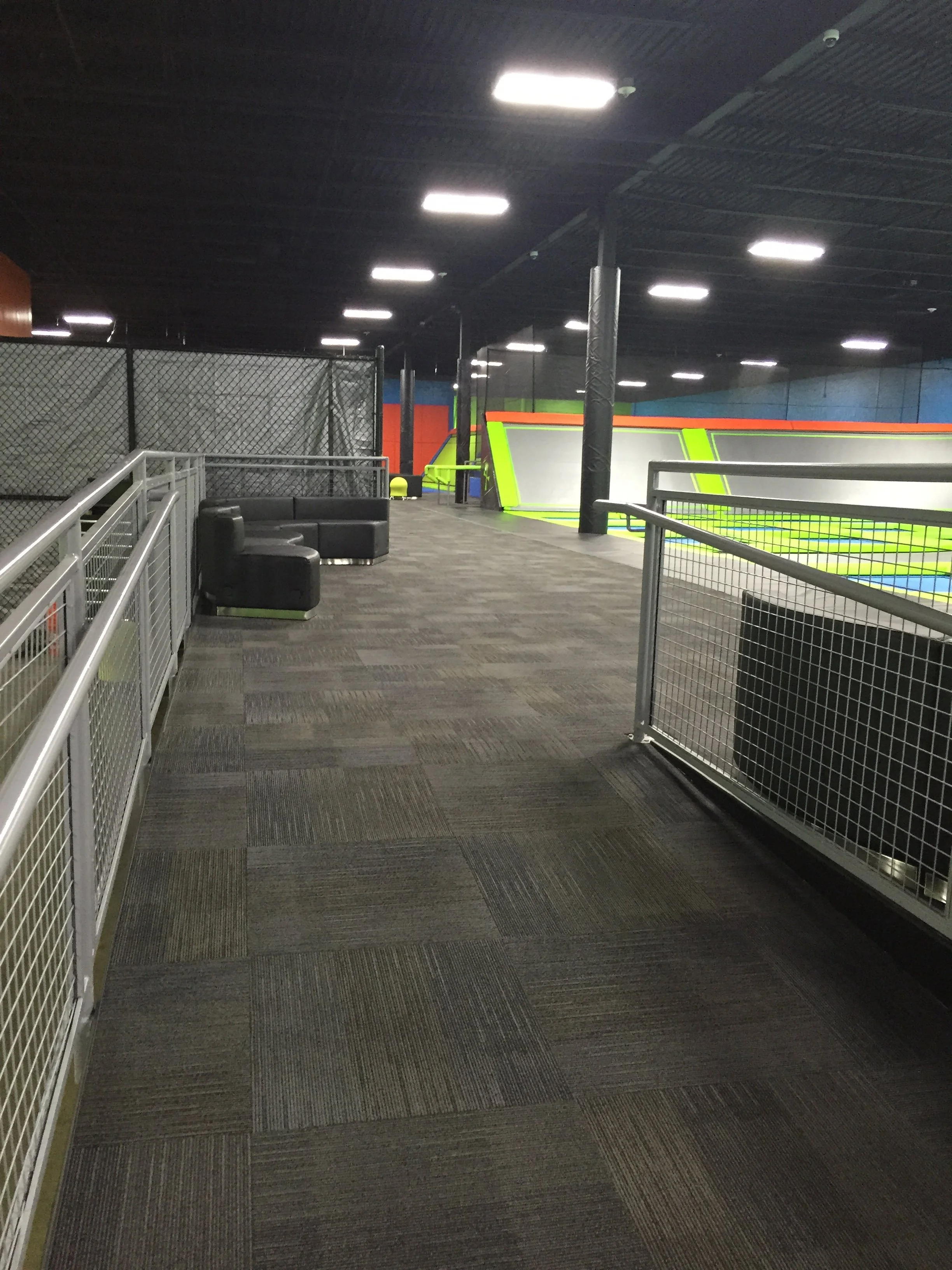 Indoor trampoline park with black ceiling, LED lights, dark carpeted floor, black and green trampoline sections, and black seating area.
