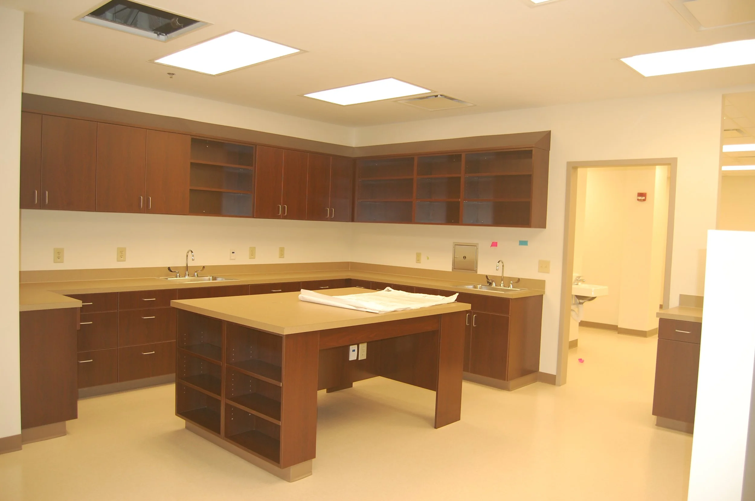 Empty modern kitchen with brown cabinets, central island, and bright ceiling lights.