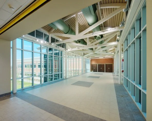 Empty indoor hallway with large windows, ceiling beams, and exposed ducts.