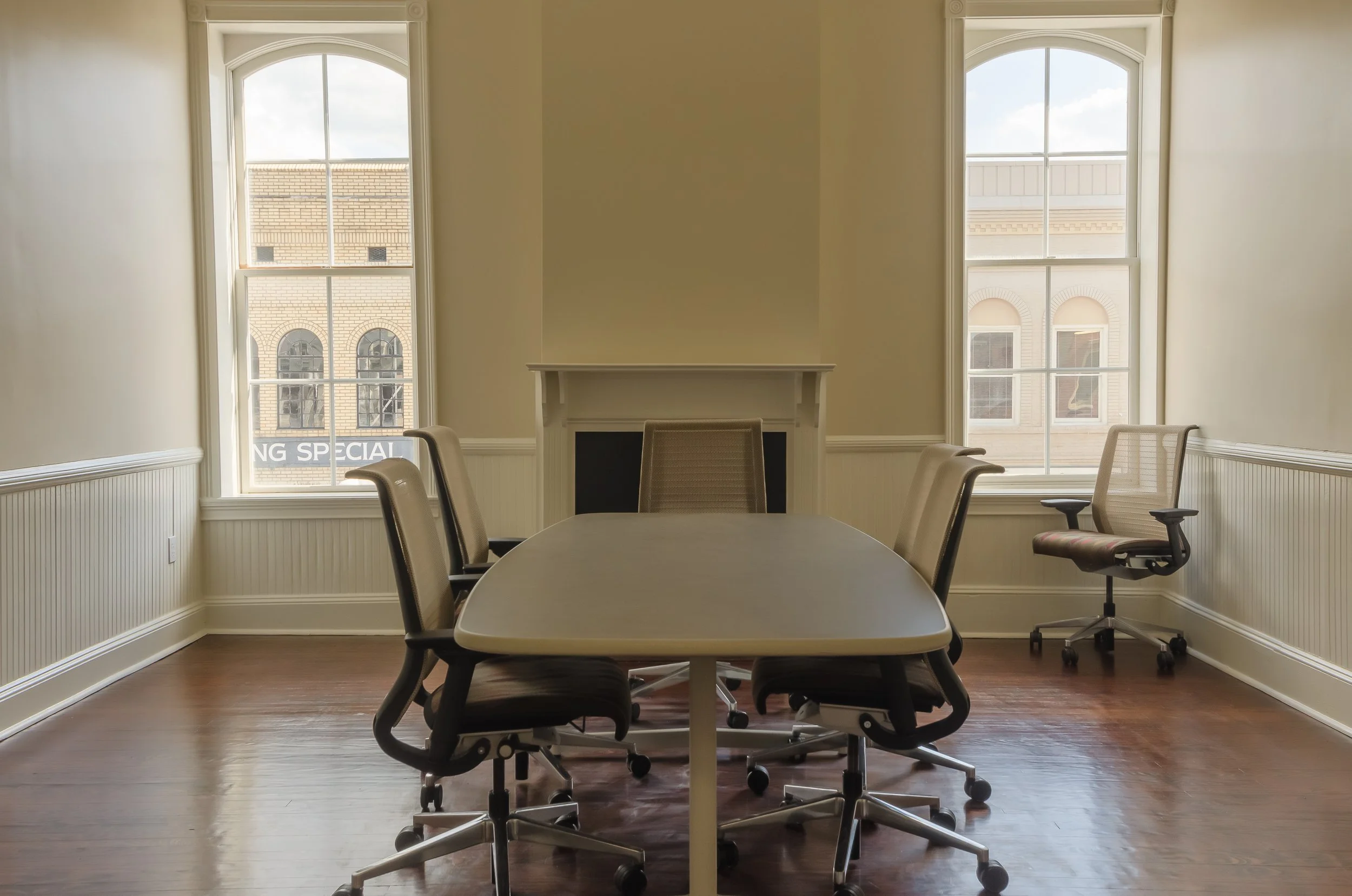 Conference room with a large table, six office chairs around it, two large windows, and a fireplace.