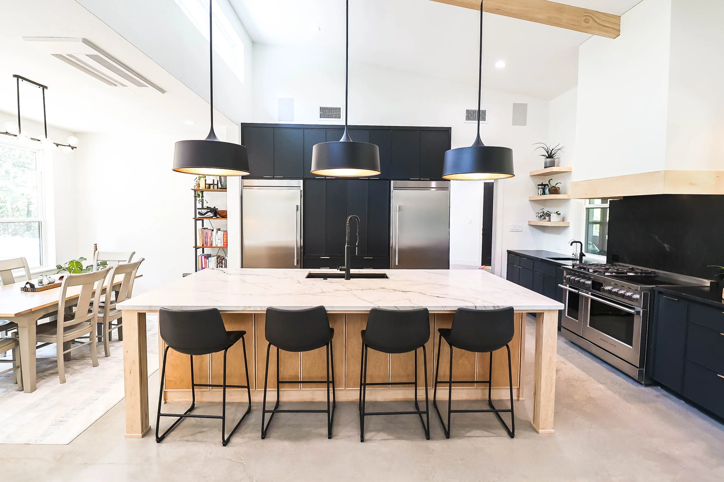 Modern kitchen with black cabinets, stainless steel appliances, and a central island with black bar stools, pendant lighting, and open shelving.
