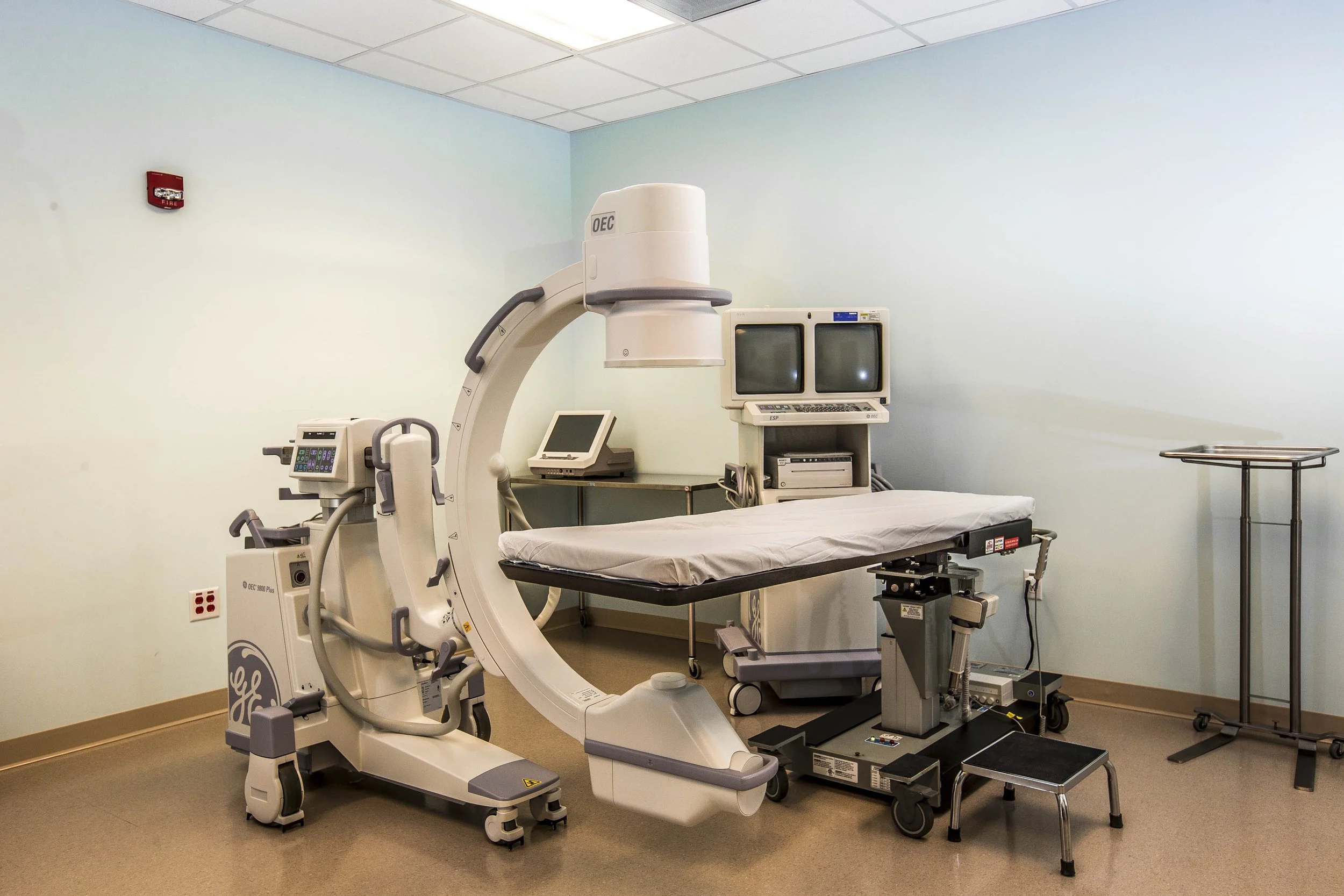 Medical imaging room with a large CT scan machine, a doctor’s bed, and several monitors and machines used for diagnostic imaging in a hospital.