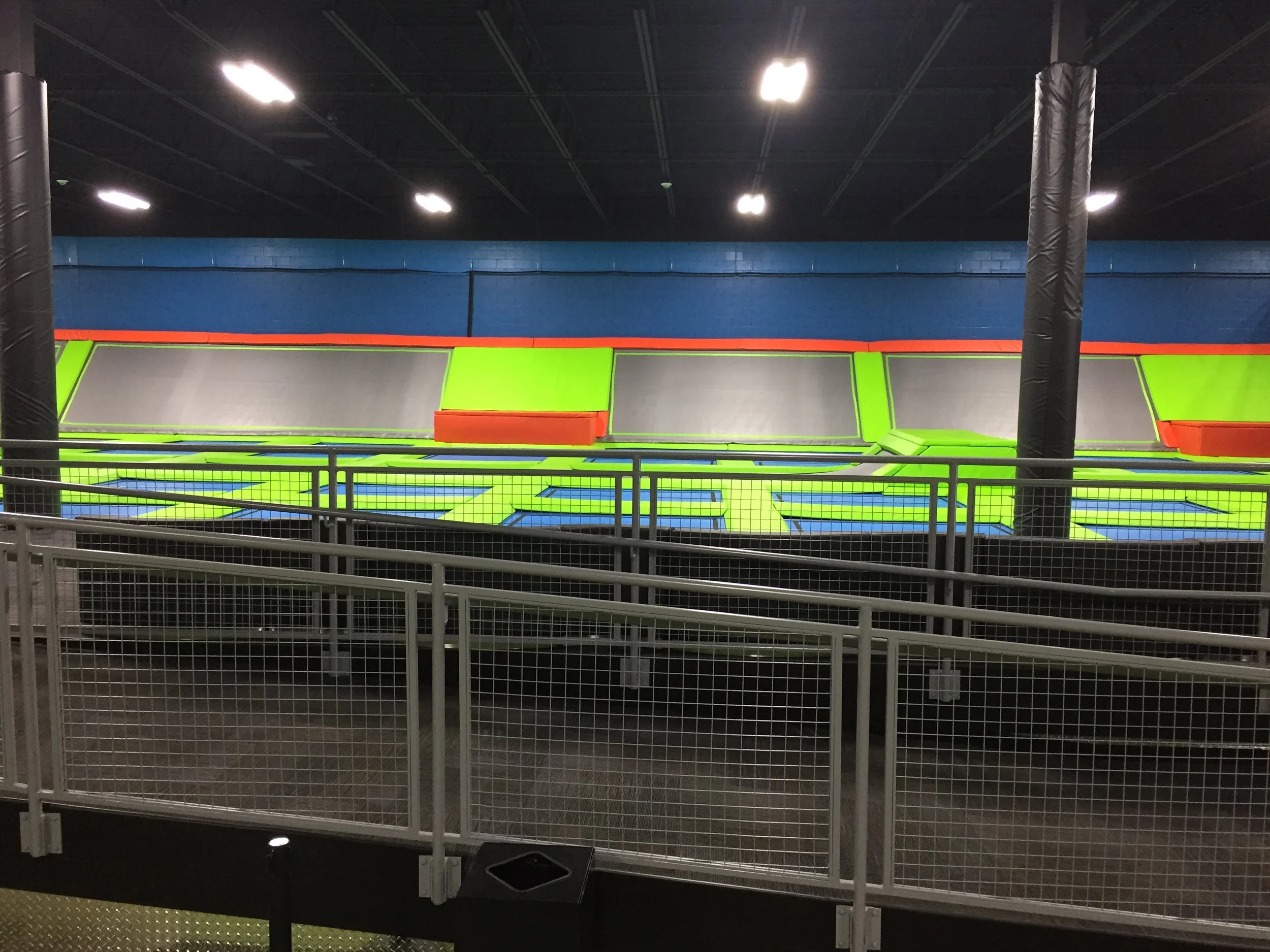 Indoor trampoline park with multiple brightly colored trampolines enclosed by white safety fences.