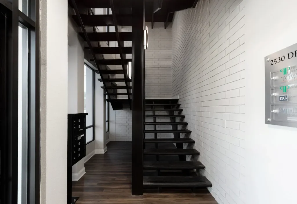 Interior of a modern building with a staircase made of black metal and dark wood steps, white brick walls, and dark wood flooring.