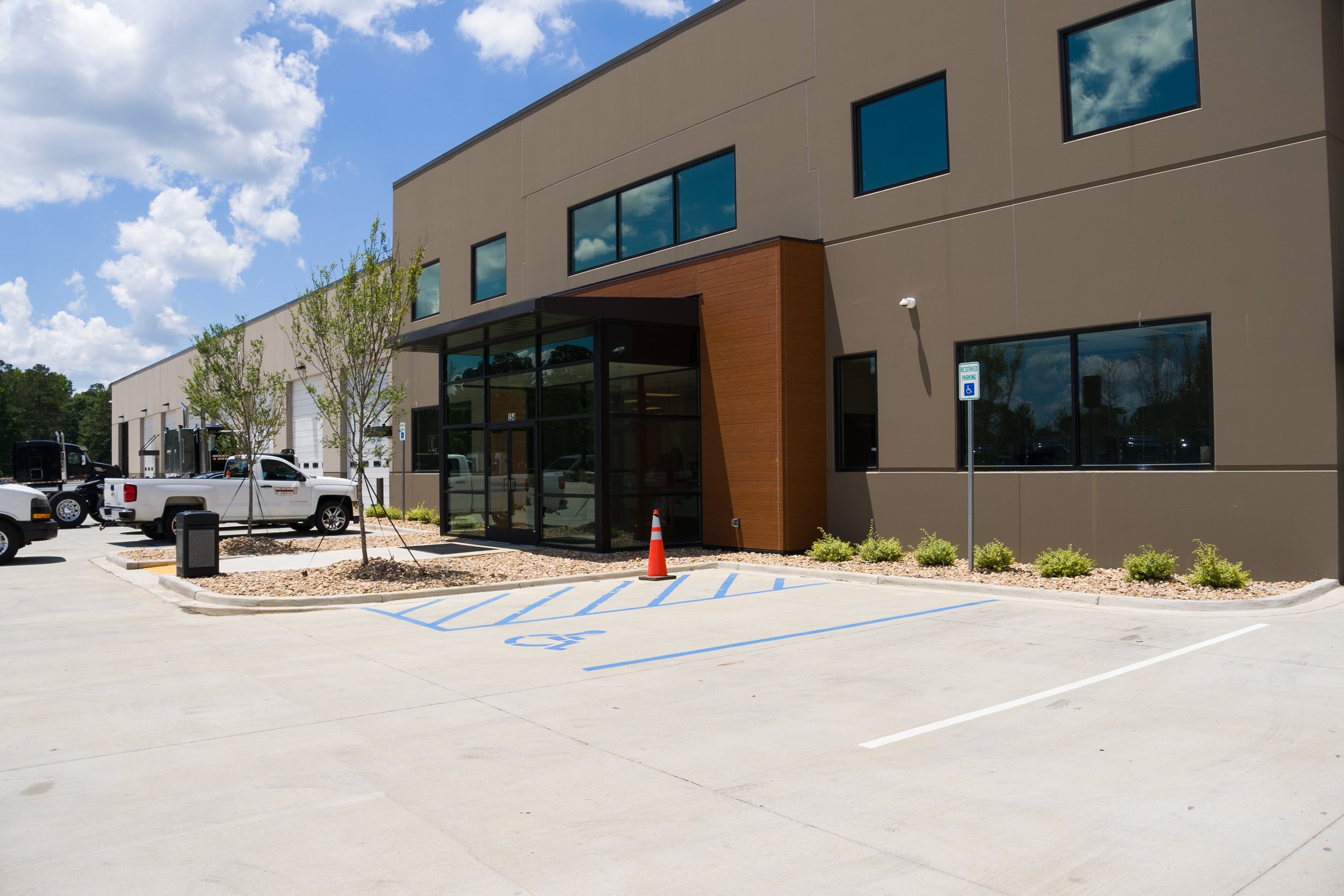Modern commercial building with large glass windows, a covered entrance, small trees, and a parking lot with several trucks and cars, including designated handicapped parking spaces.