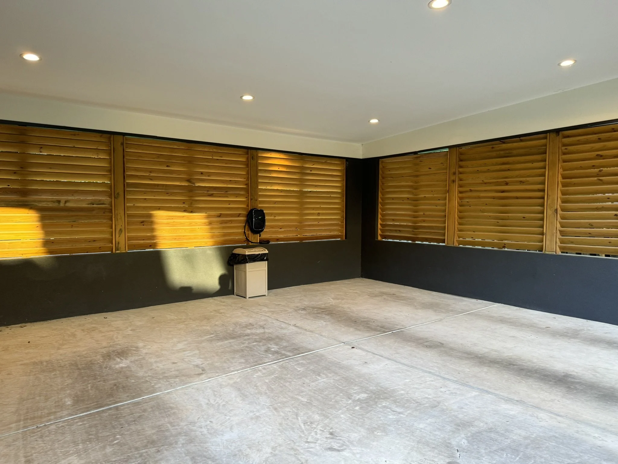 Empty room with concrete floor, wooden blinds on windows, and ceiling lights.