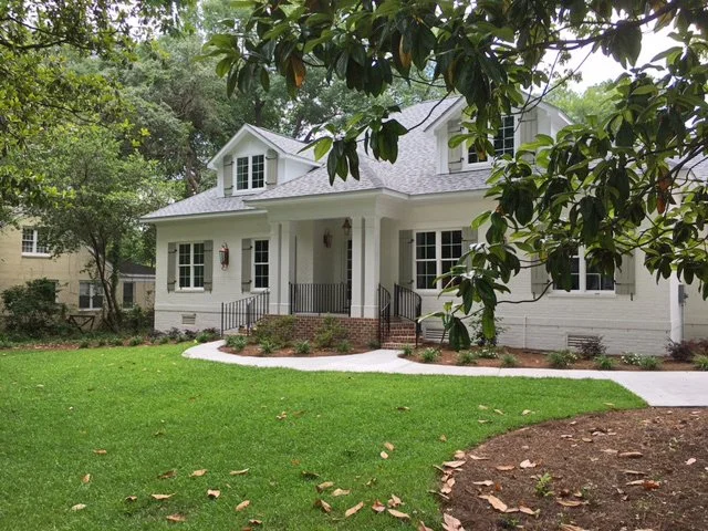 White two-story suburban house with front porch, surrounded by green lawn and trees