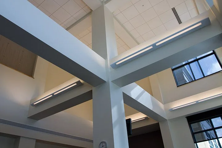 Interior view of a modern building's ceiling with intersecting white beams and large windows