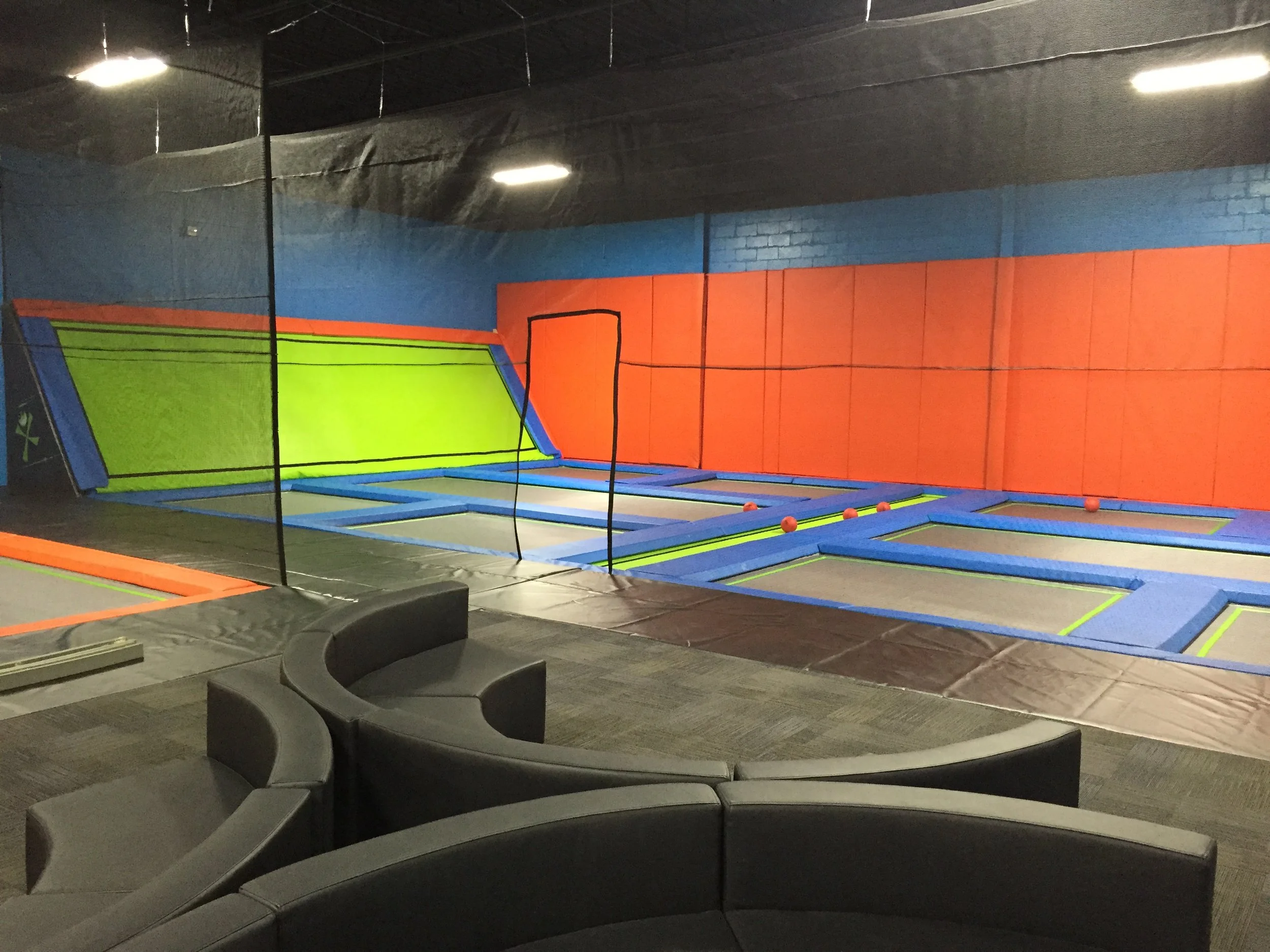 Indoor trampoline park with colorful padded walls and multiple trampolines on the floor, surrounded by a safety net.