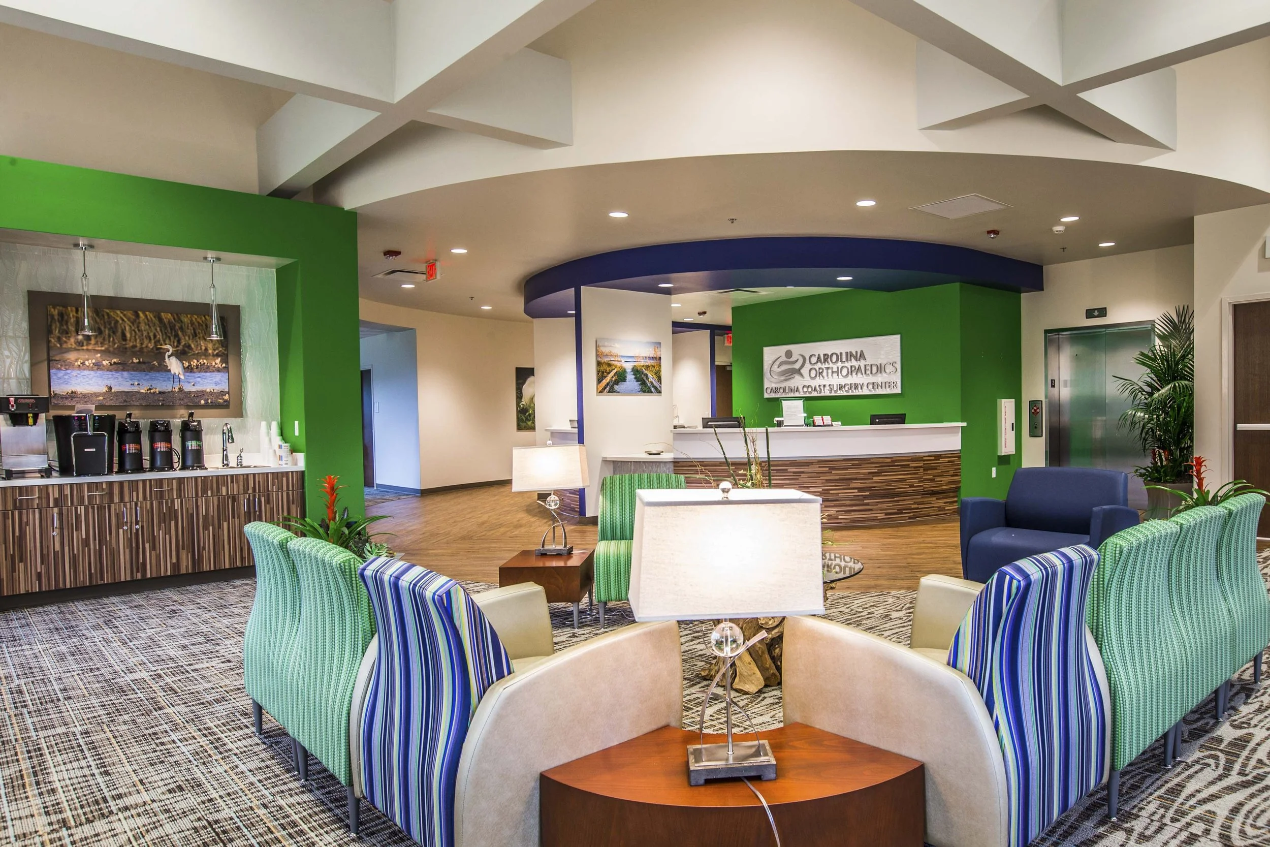 Interior of a waiting area at Carolina Orthopaedics, featuring colorful chairs, a reception desk, and decorative artwork on the walls.