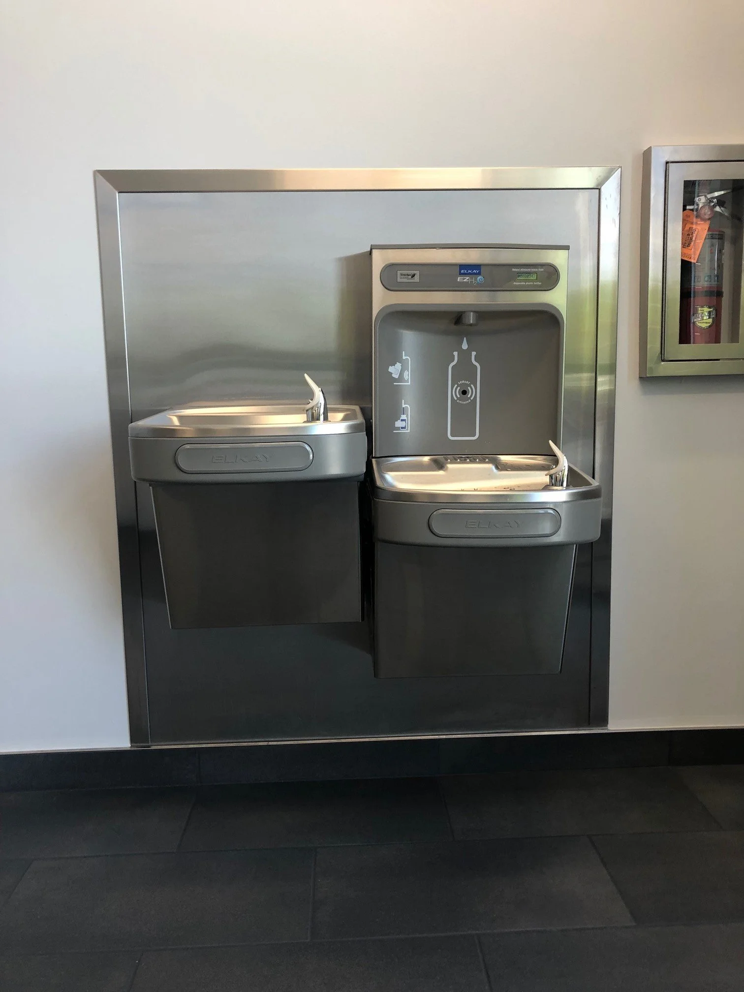 Self-service water fountain with two drinking spouts, one for regular water and one for filtered water, located in an indoor setting.
