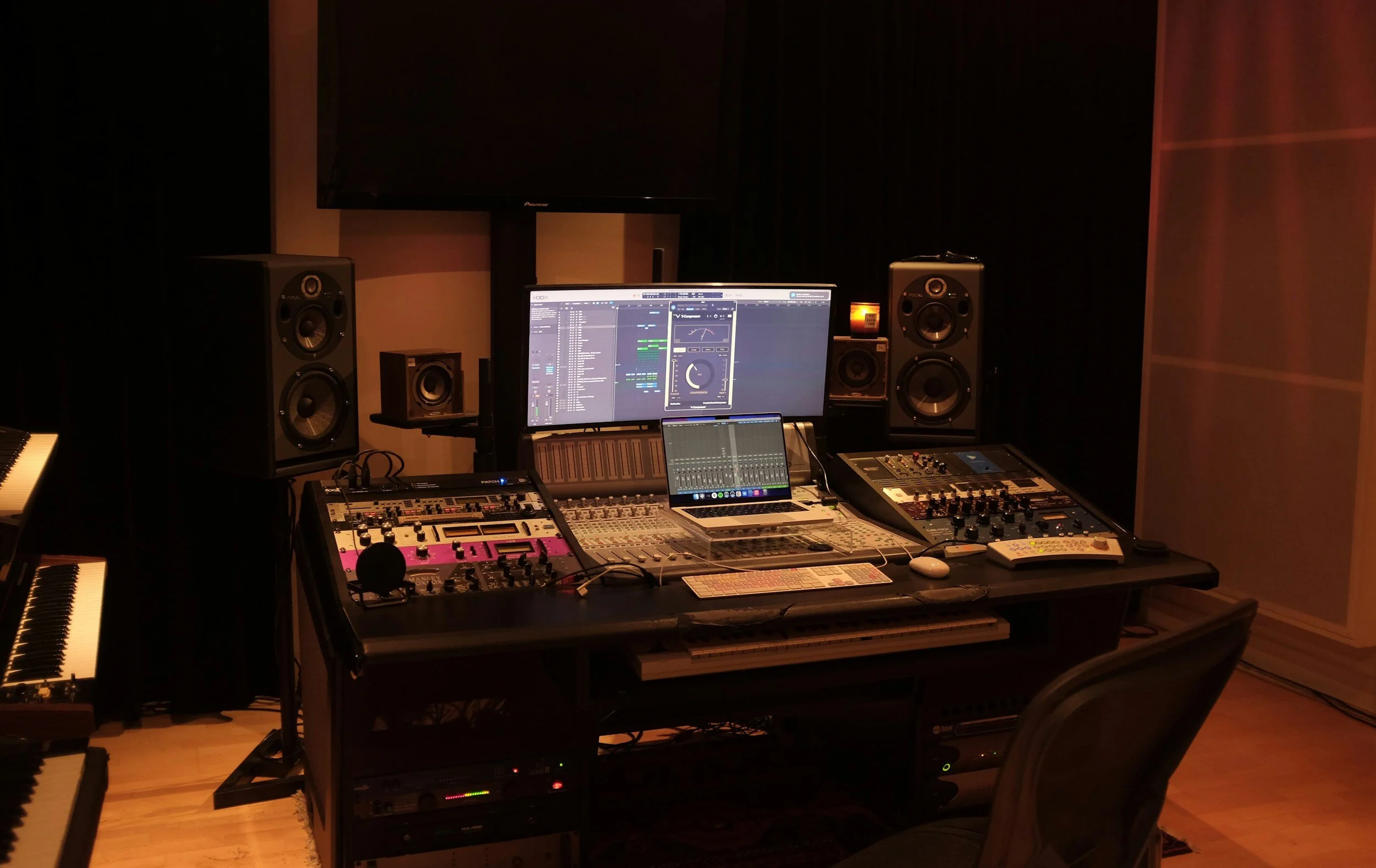 A music studio filled with audio equipment including speakers, a computer, mixing consoles, and other electronic music production gear.