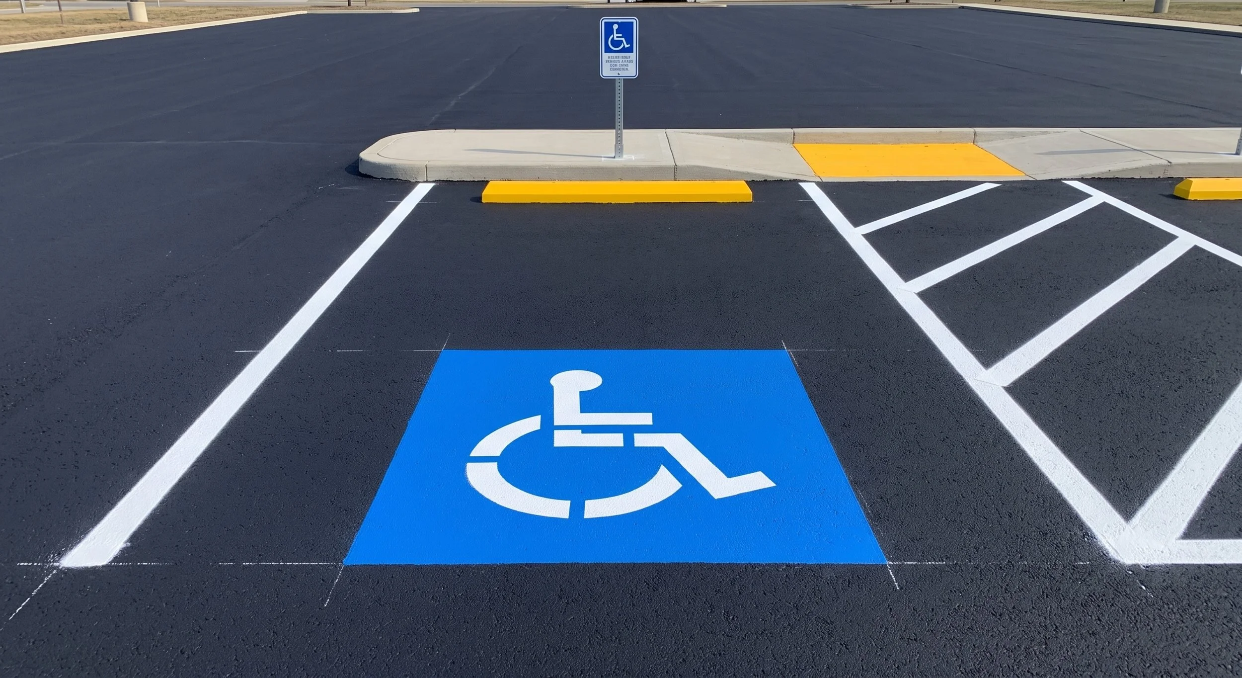 A parking space designated for handicapped accessibility, marked by a blue wheelchair symbol painted on the asphalt and a blue signpost with a wheelchair icon, situated next to a curb ramp with yellow safety markings.