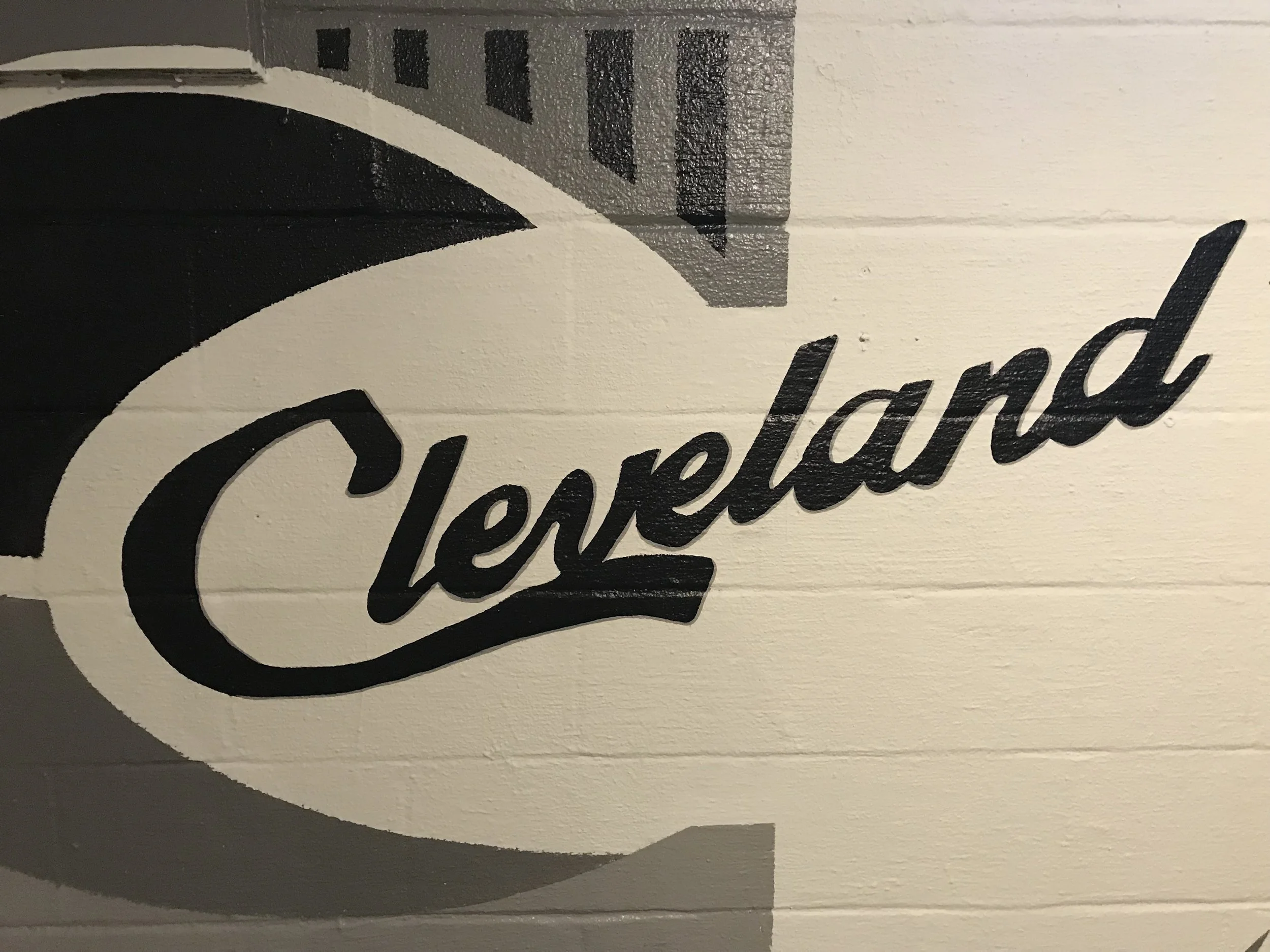 Part of a painted sign or mural with black and gray text on a white wall, with a partially visible black curved design.