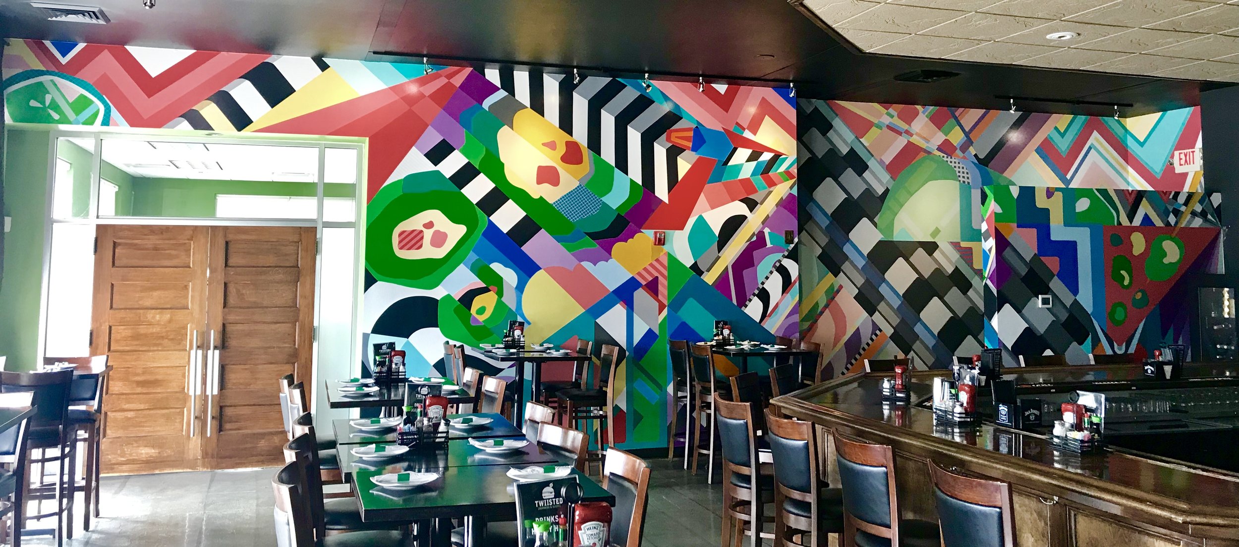 Colorful abstract mural wall in a restaurant with tables and chairs set for dining.
