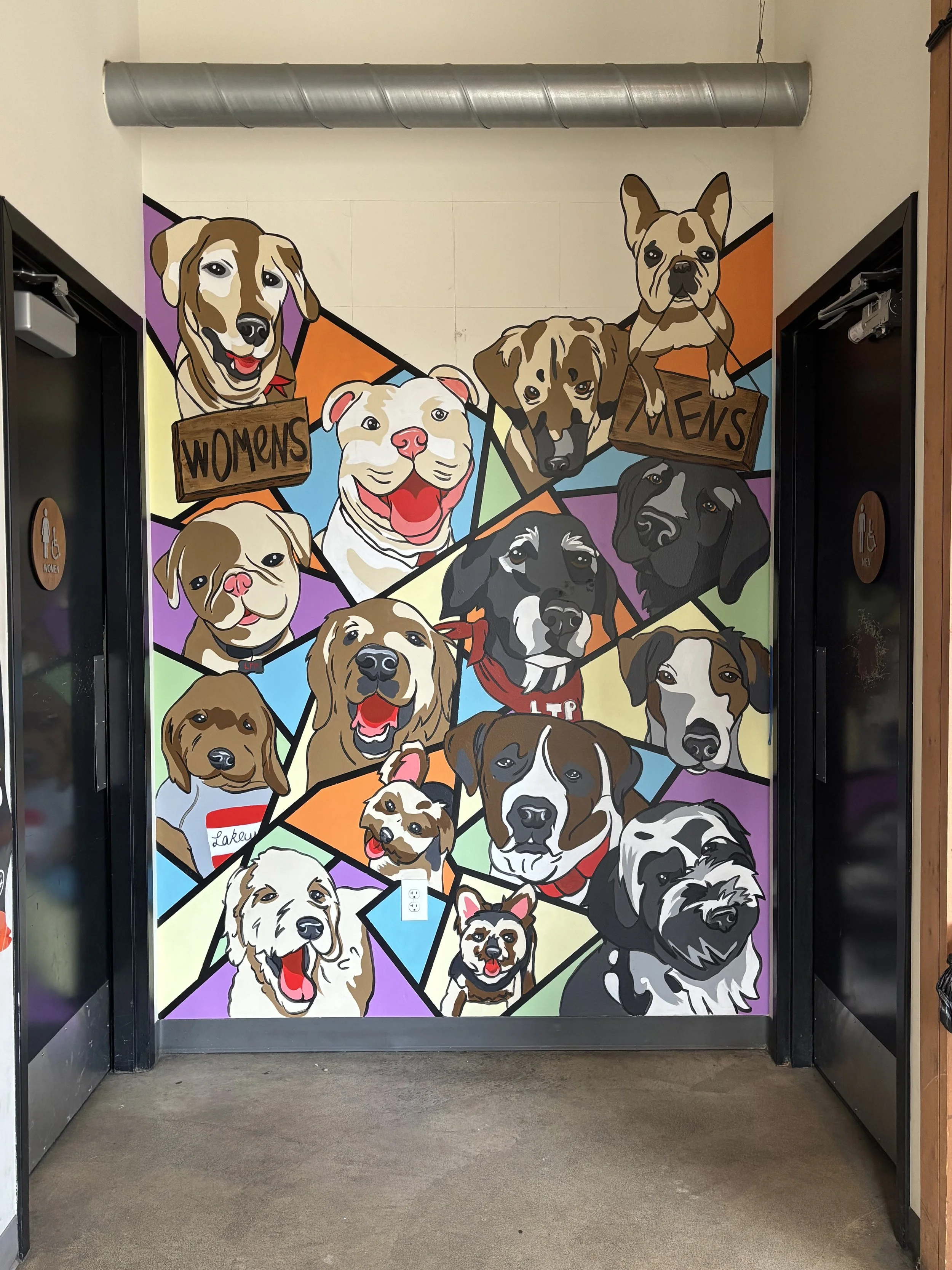 Colorful mural of various dog breeds on a wall, with two doors on each side labeled for women's and men's restrooms.