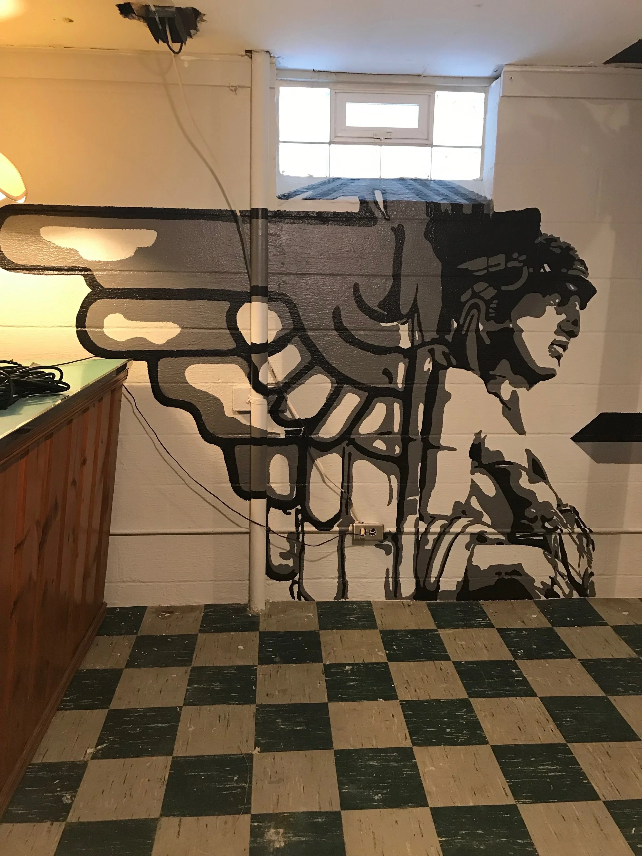 Wall art depicting a person with headphones, in black and white, in a room with checkered black and beige tile flooring, a wooden cabinet, and a window with a blue and black striped curtain.