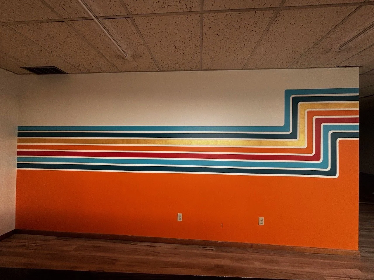 Wall mural with a retro geometric design featuring horizontal lines in shades of blue, orange, red, and yellow on an orange background.