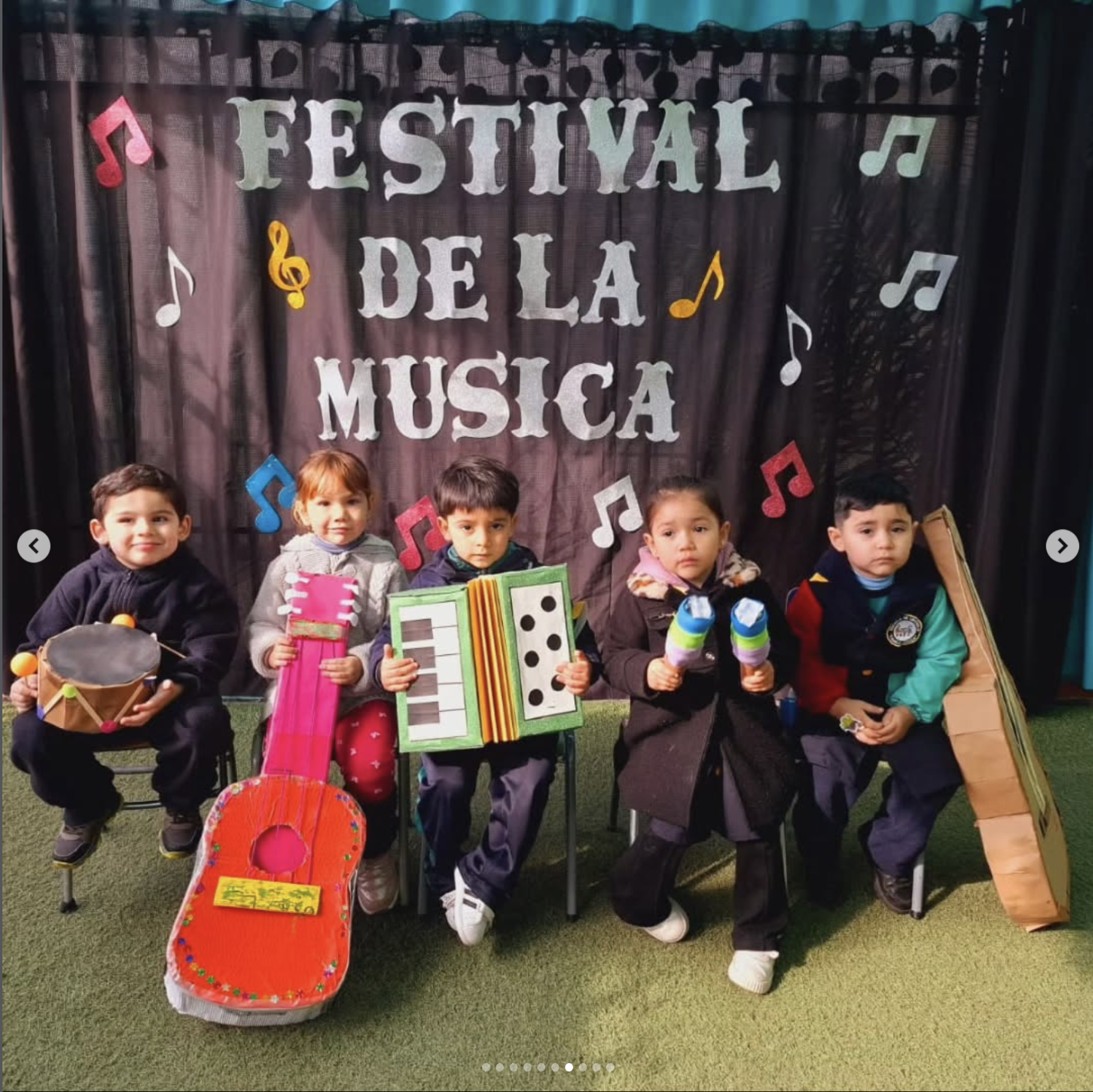 Grupo de niños sosteniendo instrumentos musicales en un escenario con un toldo azul y un telón con letras que dicen 'Festival de la Música' rodeados de notas musicales decorativas.